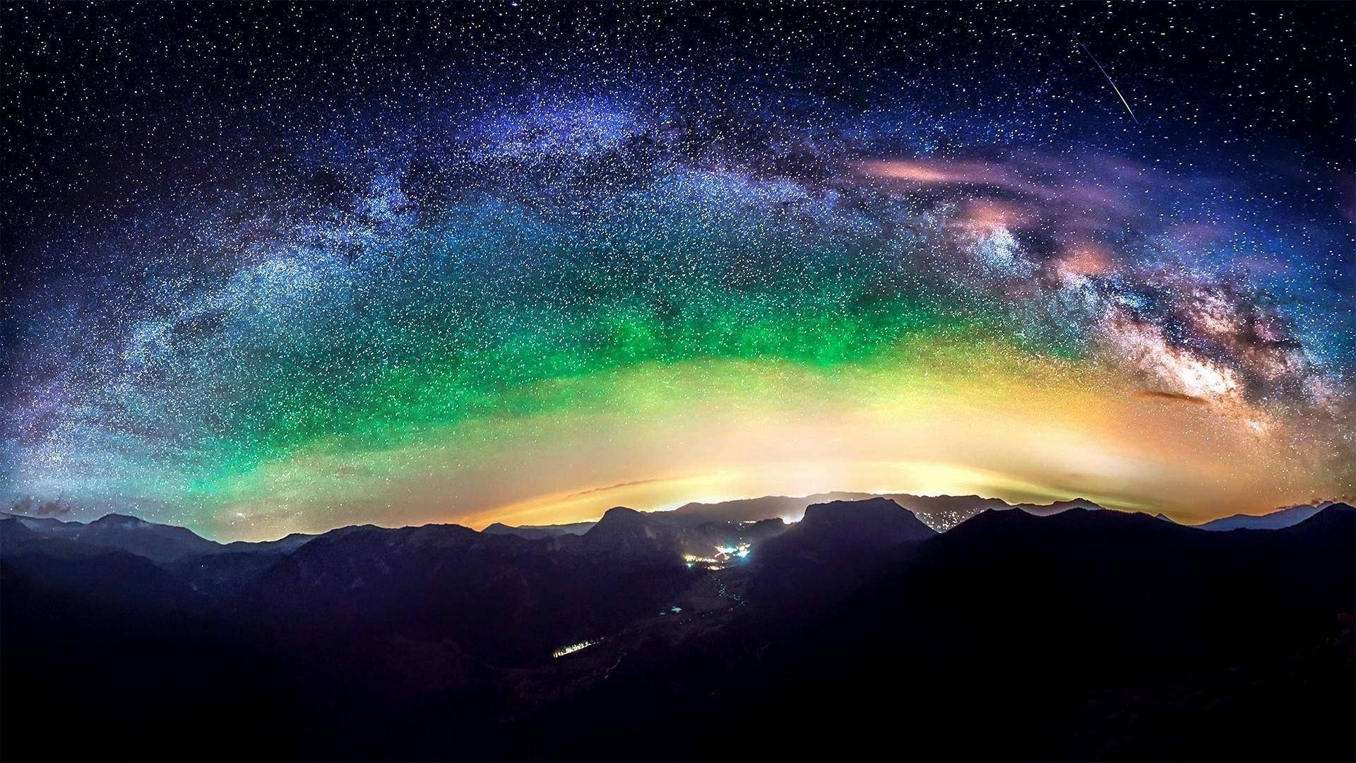 銀河 live 桌布 壁紙 — 山頂上令人驚嘆的夜空，銀河在繁星點點的廣闊天空中閃耀著鮮豔的綠色和紫色。