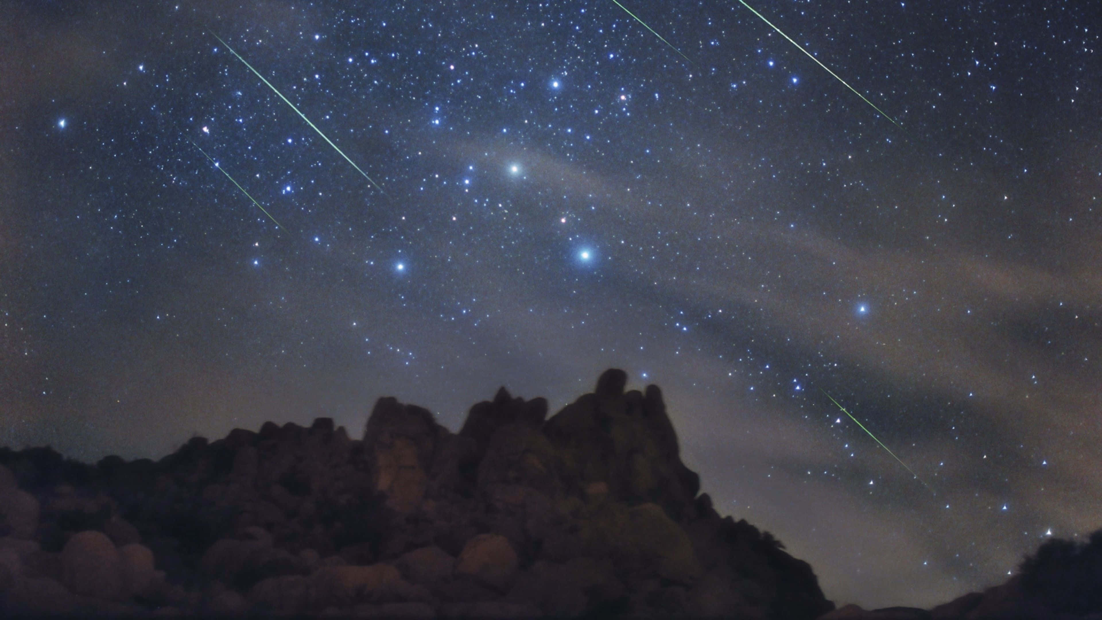Silhouette 桌布 壁紙 — 岩石山脈剪影，背景是繁星點點的夜空，劃過發光流星痕跡。