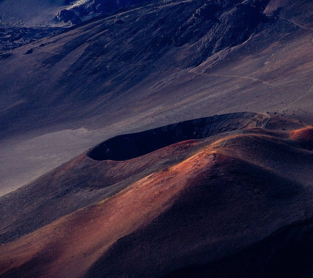 Volcano 桌布 壁紙 — 崎嶇地形上，火山口邊緣散發溫暖橙色光芒，與冷藍色陰影形成對比的航拍視圖。