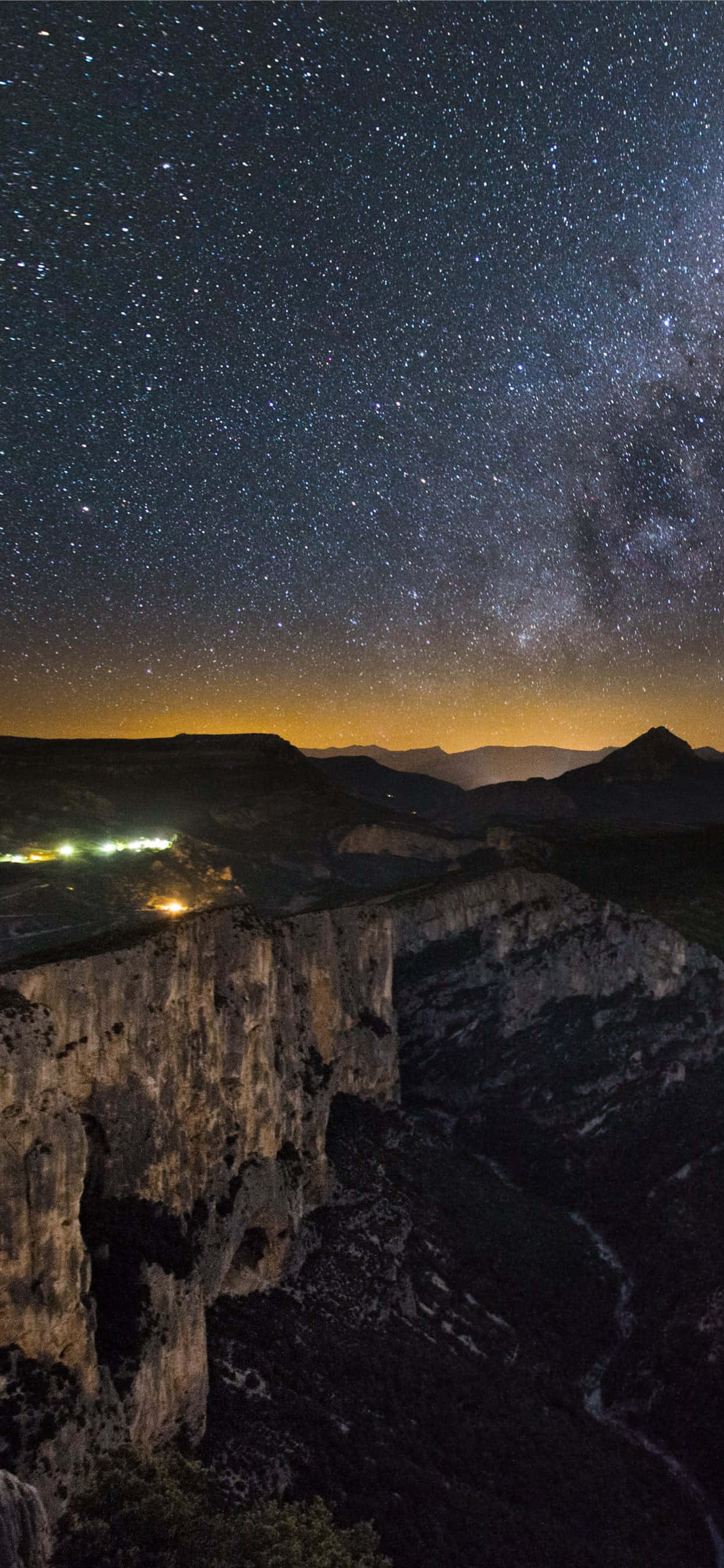 桌布 壁紙 — 崎嶇山峽上方滿天星斗的夜空，下方遠處燈火點點，令人嘆為觀止的夜景。