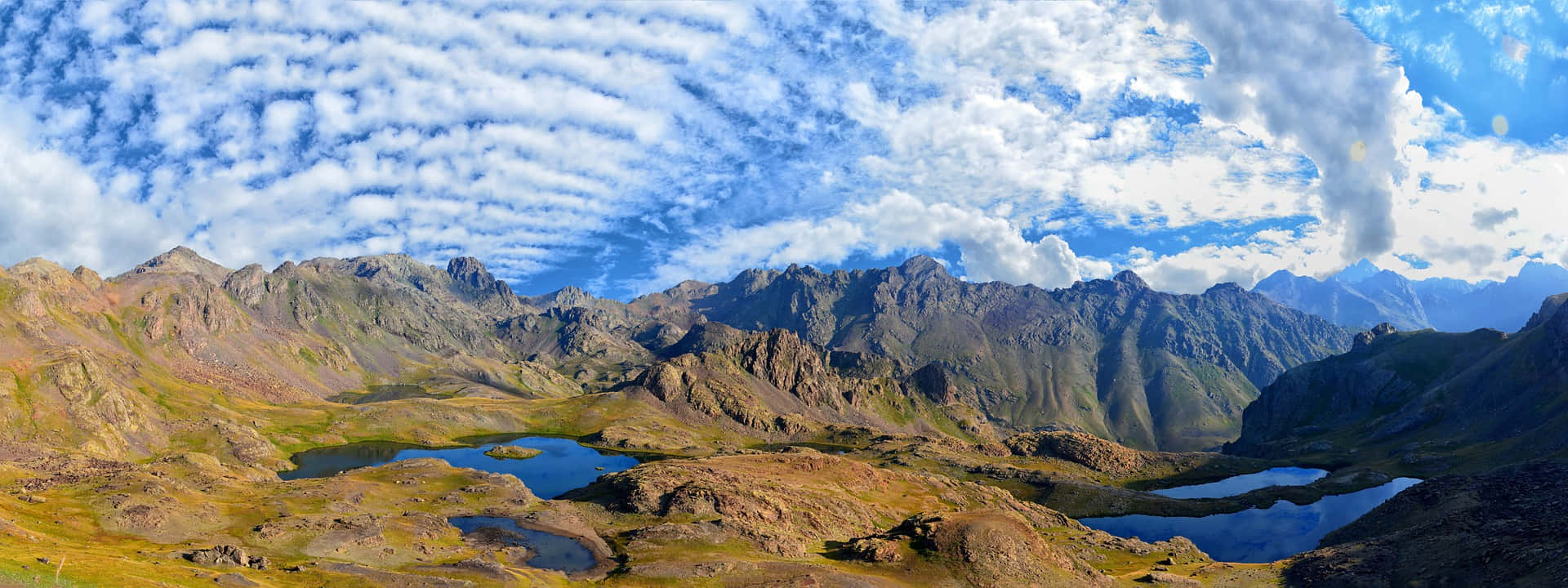 Blue Sky 桌布 壁紙 — 崎嶇山脈的全景視野，有鋸齒狀山峰和高山湖泊，映照著蔚藍天空和縷縷白雲。