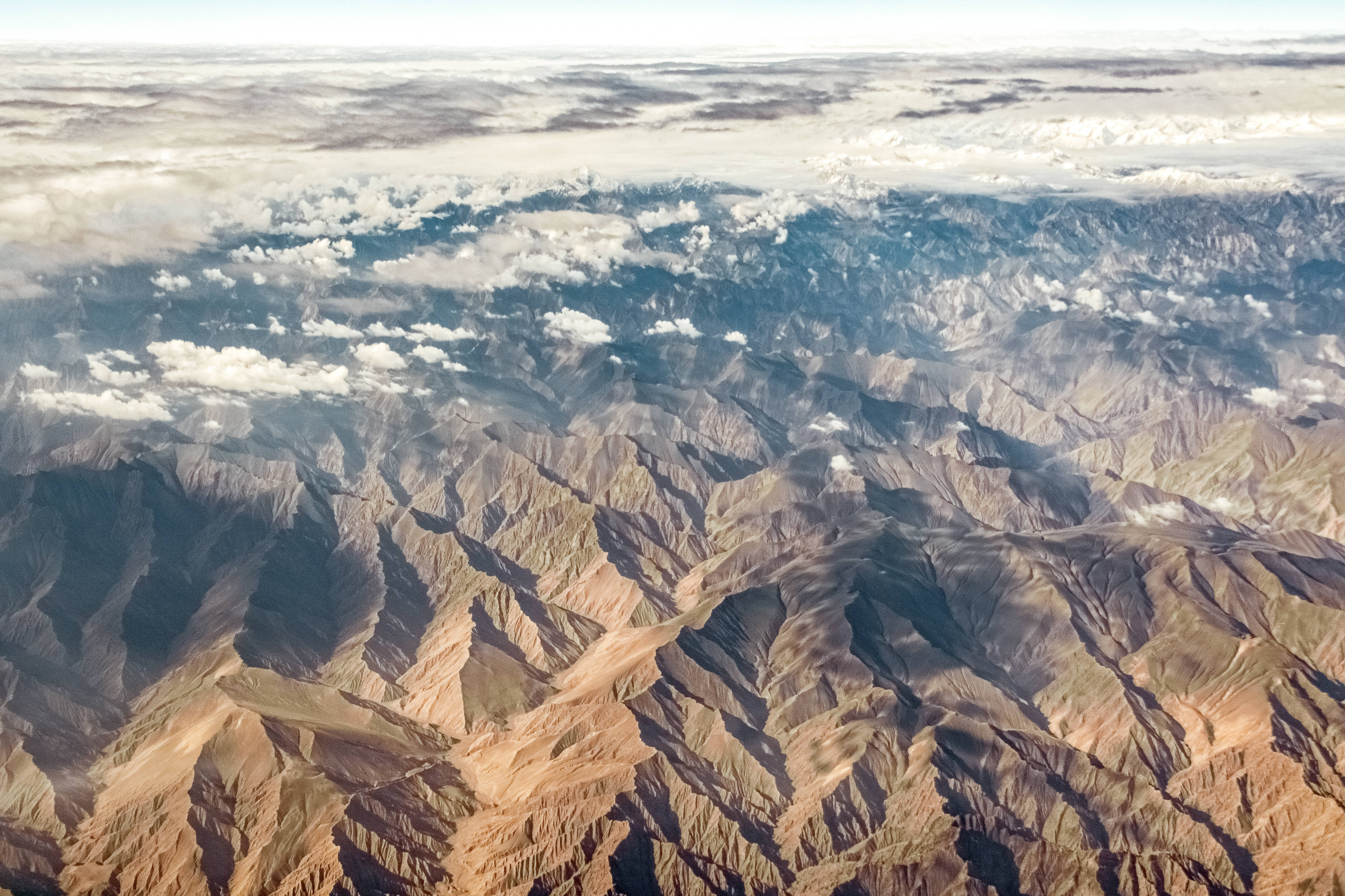 Topography 桌布 壁紙 — 崎嶇山脈的鳥瞰圖，有深谷和下方散落的雲層。
