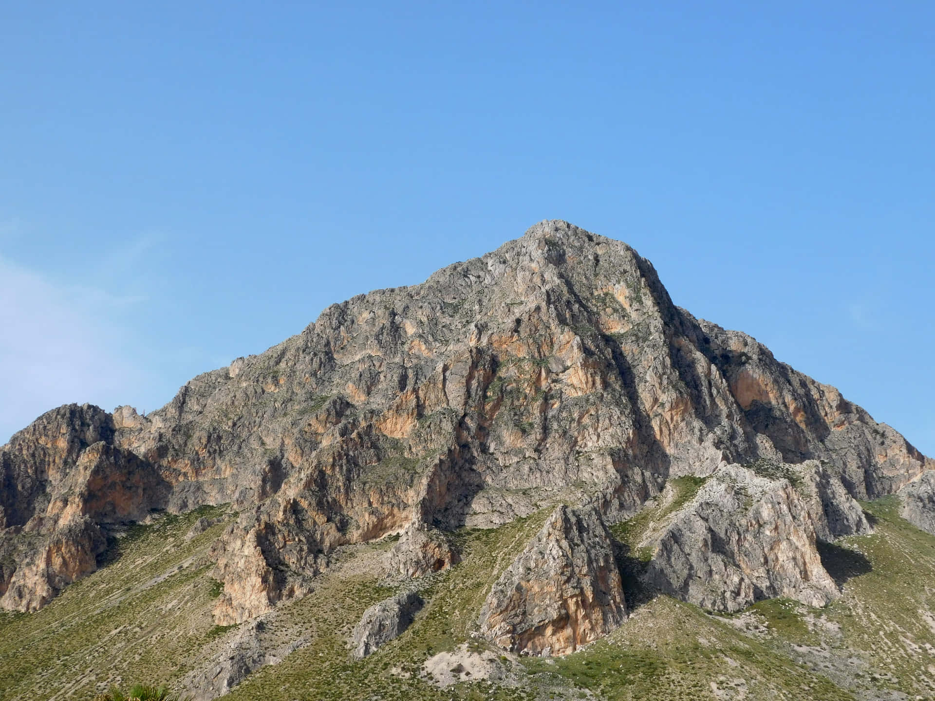 Mountain 壁紙 — 崎嶇岩石山峰在清澈藍天下陡峭聳立，山坡上稀疏的綠色植被緊貼其上。