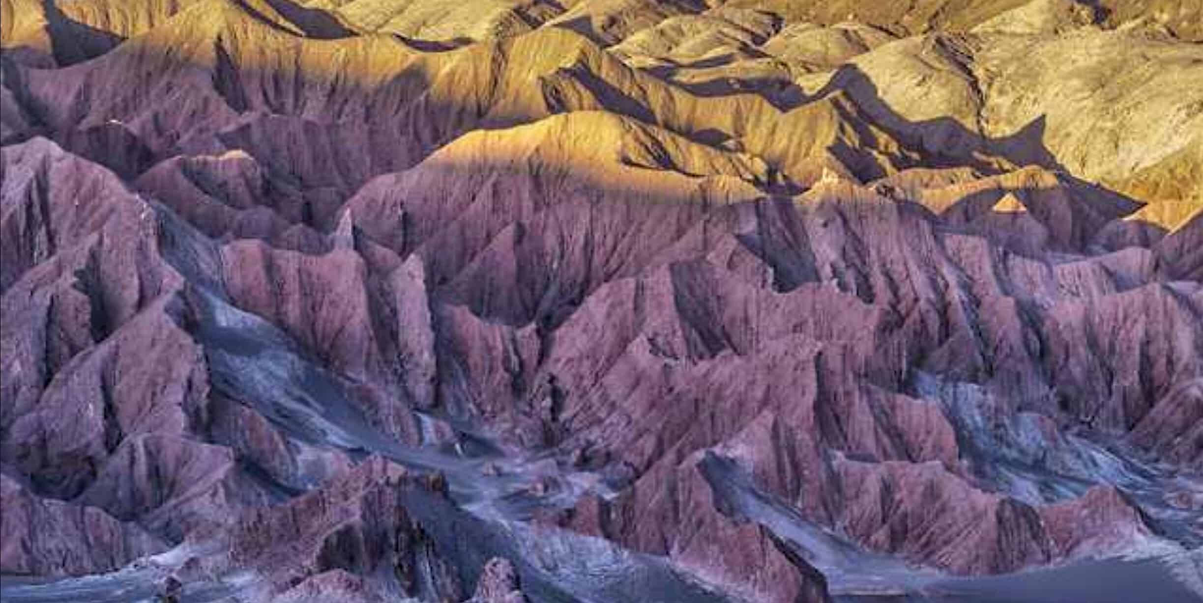 iPad Pro 桌布 壁紙 — 崎嶇峽谷的鳥瞰圖，紫色和金色的岩層沐浴在溫暖的日落光線中。