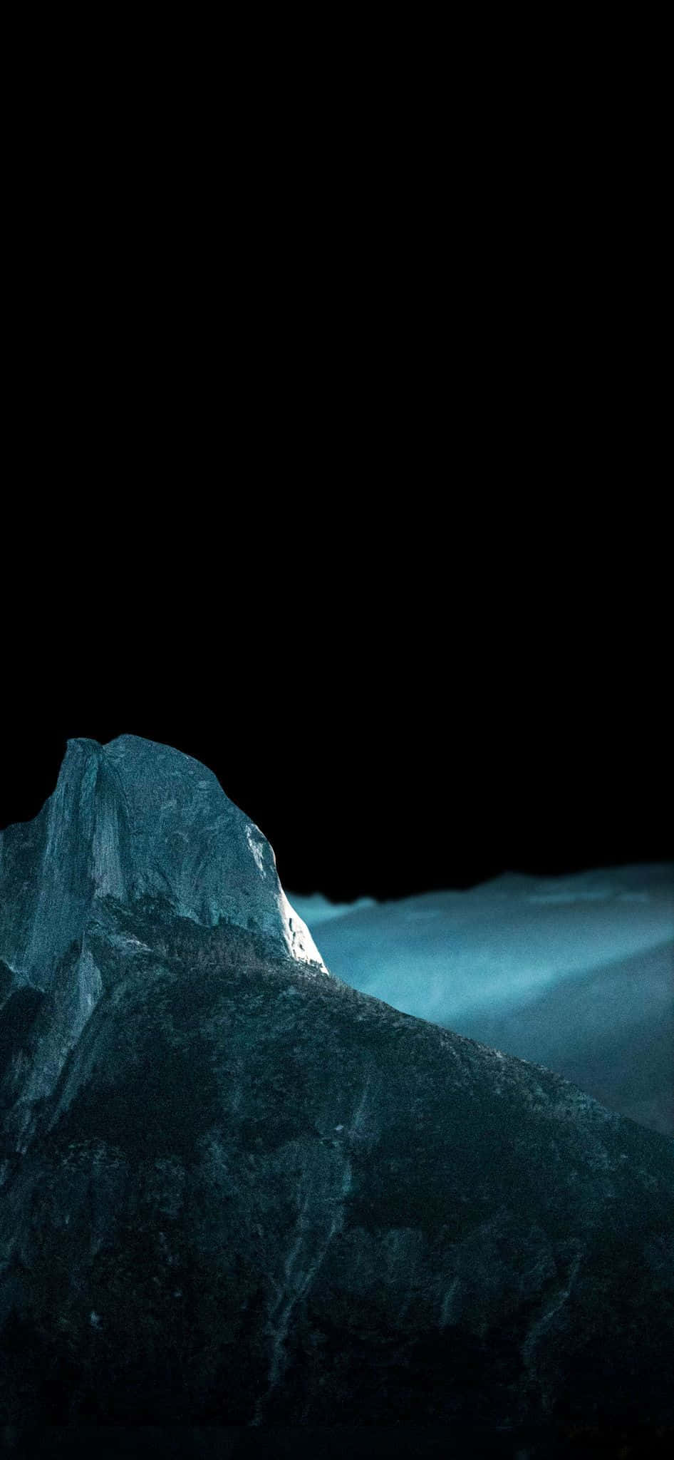 OLED 桌布 壁紙 — 崎嶇的山峰在漆黑的天空和霧氣瀰漫的山谷上方散發出冷藍色的光芒。