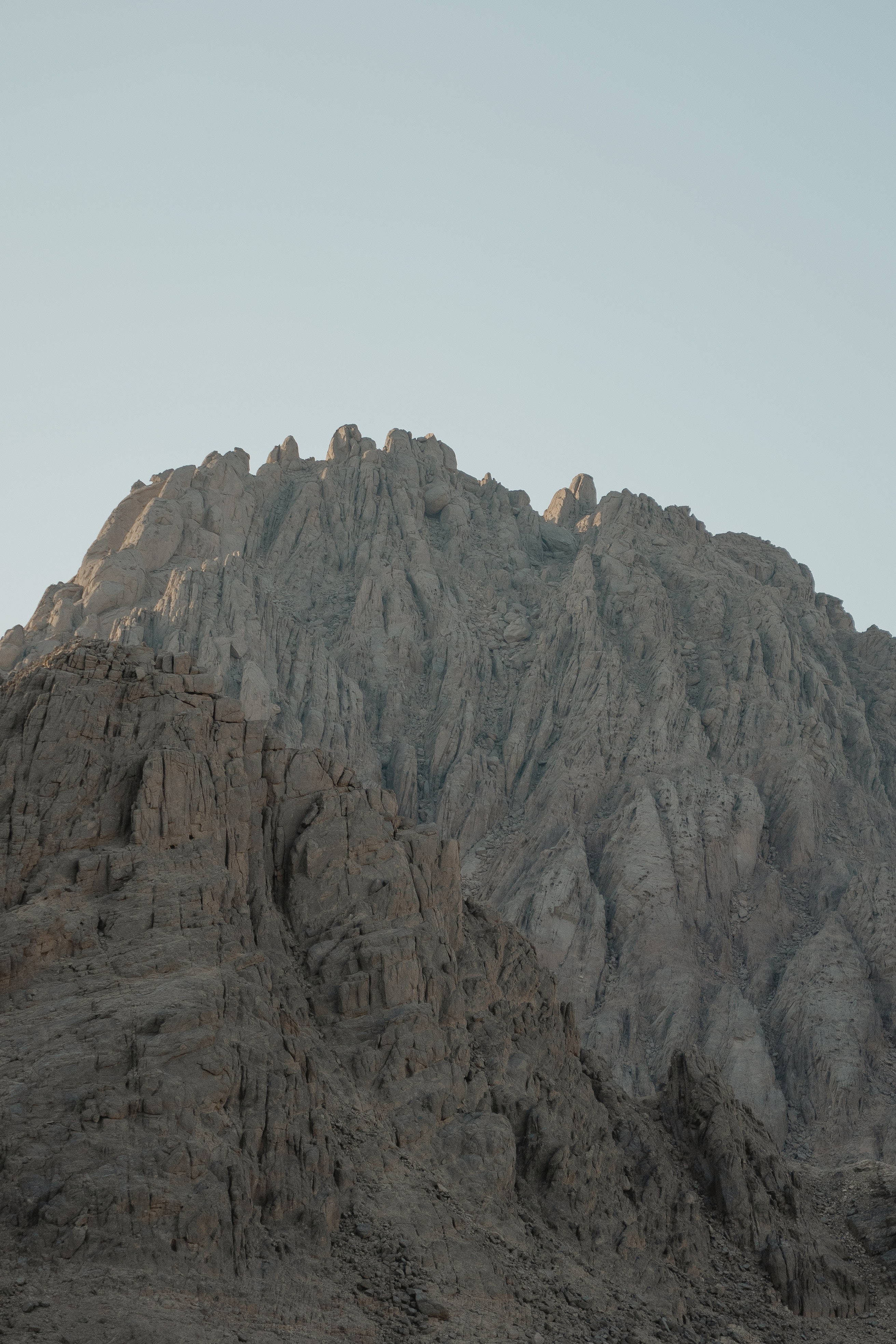 Egypt 桌布 壁紙 — 崎嶇的岩石山峰在淡色天空下尖銳地聳立，柔和的金色光線突出了其鋸齒狀的山脊。