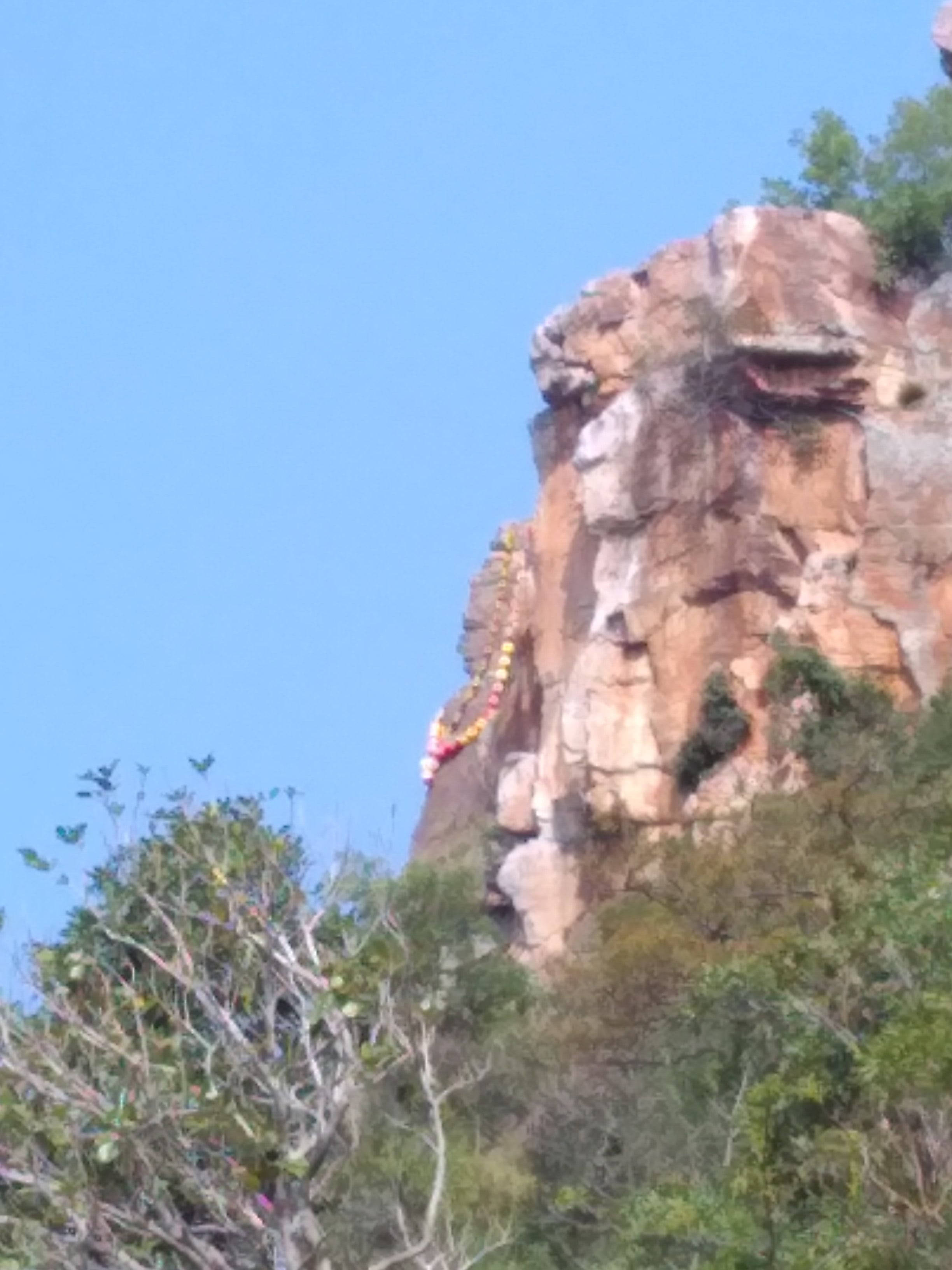 山景 桌布 壁紙 — 崎嶇的懸崖面上裝飾著色彩繽紛的經幡，映襯著清澈的藍天和茂密的綠樹。