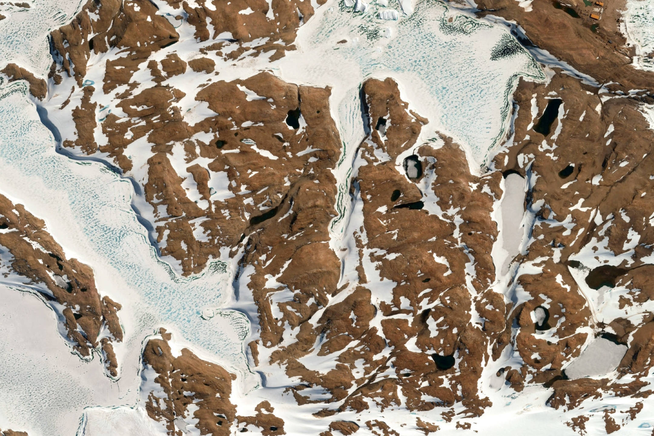Google 地球 桌布 壁紙 — 崎嶇的棕色山脈部分被冰雪覆蓋，蜿蜒的融水溪流的鳥瞰圖。