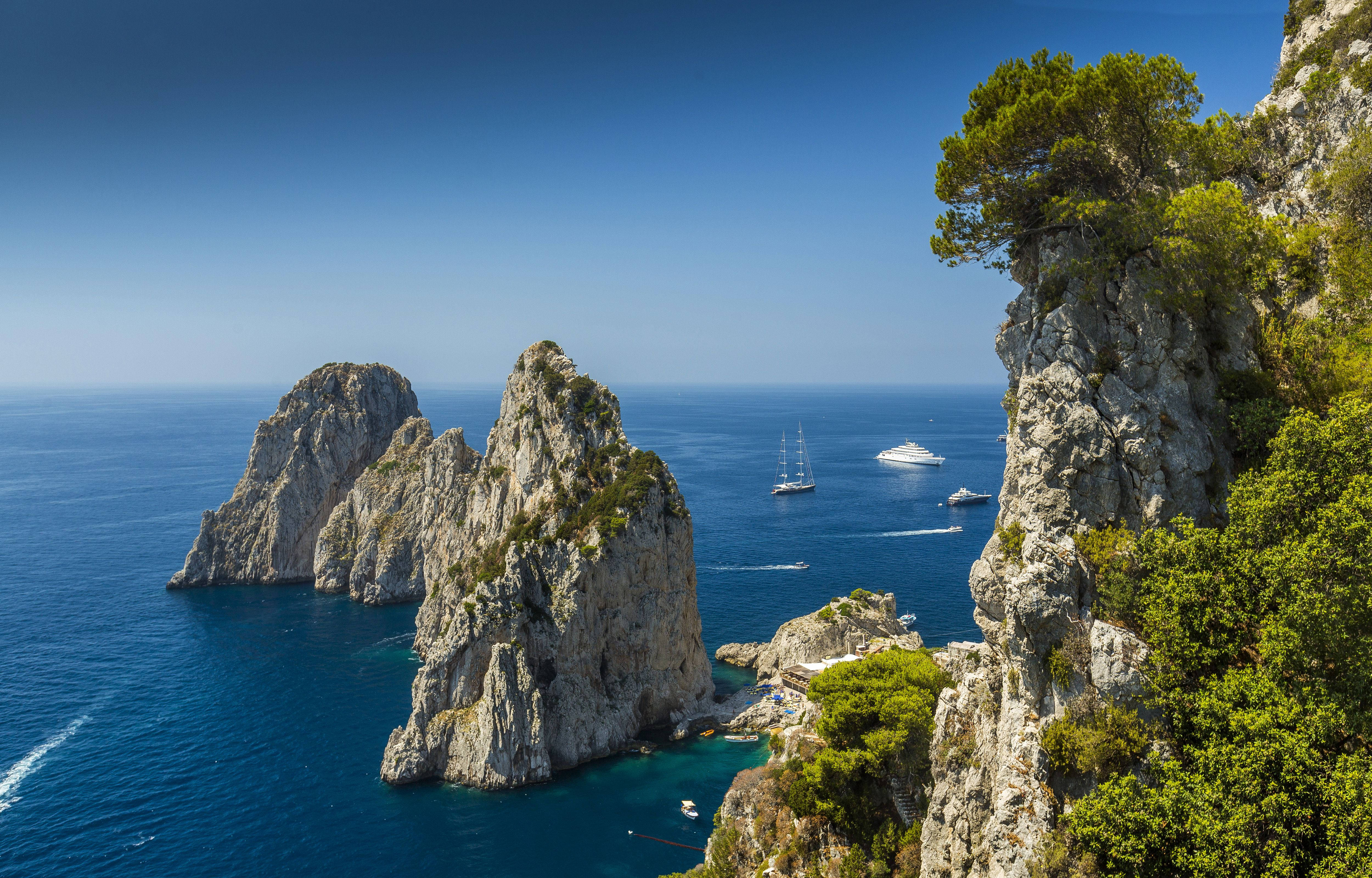Capri 桌布 壁紙 — 崎嶇的石灰岩懸崖插入充滿活力的碧綠海水，在晴朗的藍天下，帆船在附近漂流。