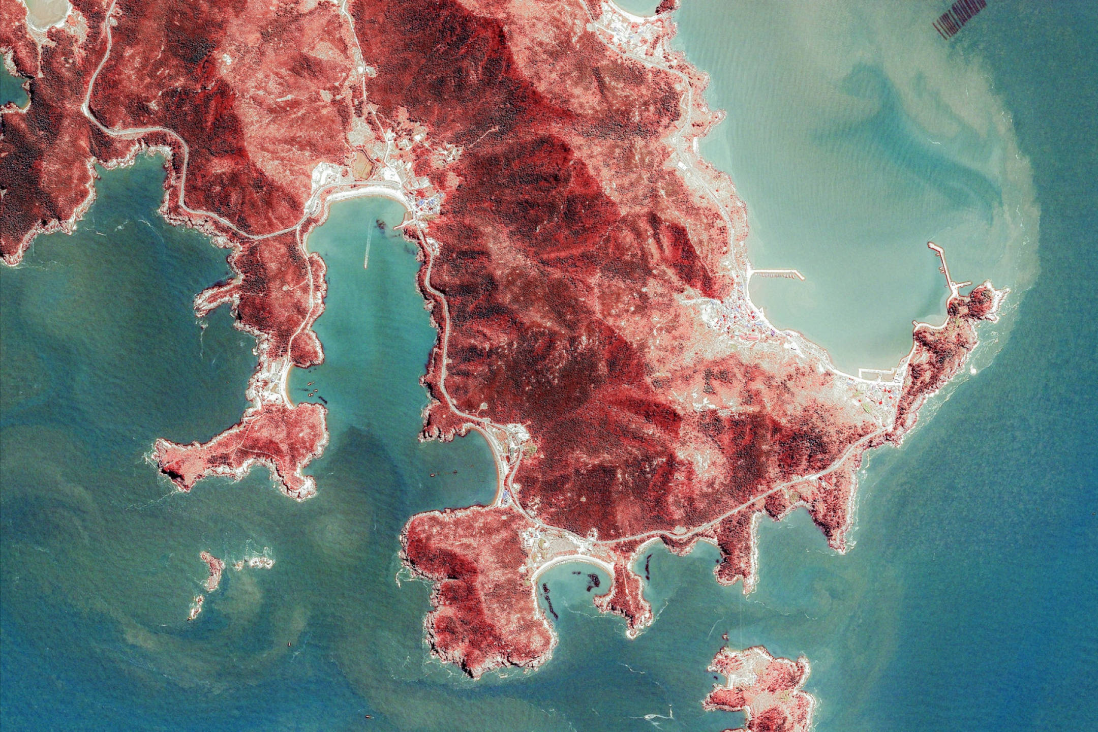 Google 地球 桌布 壁紙 — 崎嶇的紅土海岸線延伸至碧綠海水，蜿蜒的白色道路縱橫其間的鳥瞰圖。