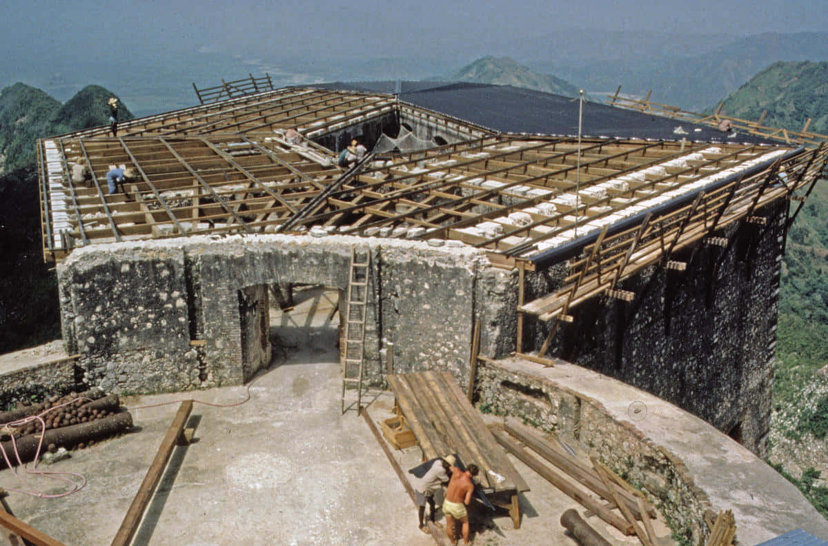 Fortress 桌布 壁紙 — 工人在山頂的石造建築上建造木屋頂，遠方有翠綠的山丘，天空朦朧。