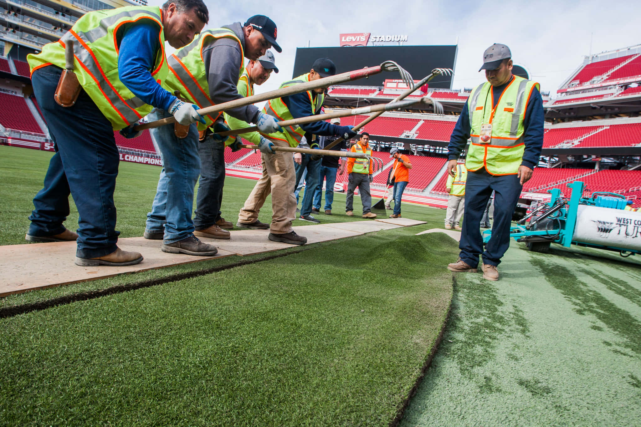 足球 桌布 壁紙 — 工人穿著亮色背心，在陰天時於Levi's Stadium的足球場上安裝人造草皮。