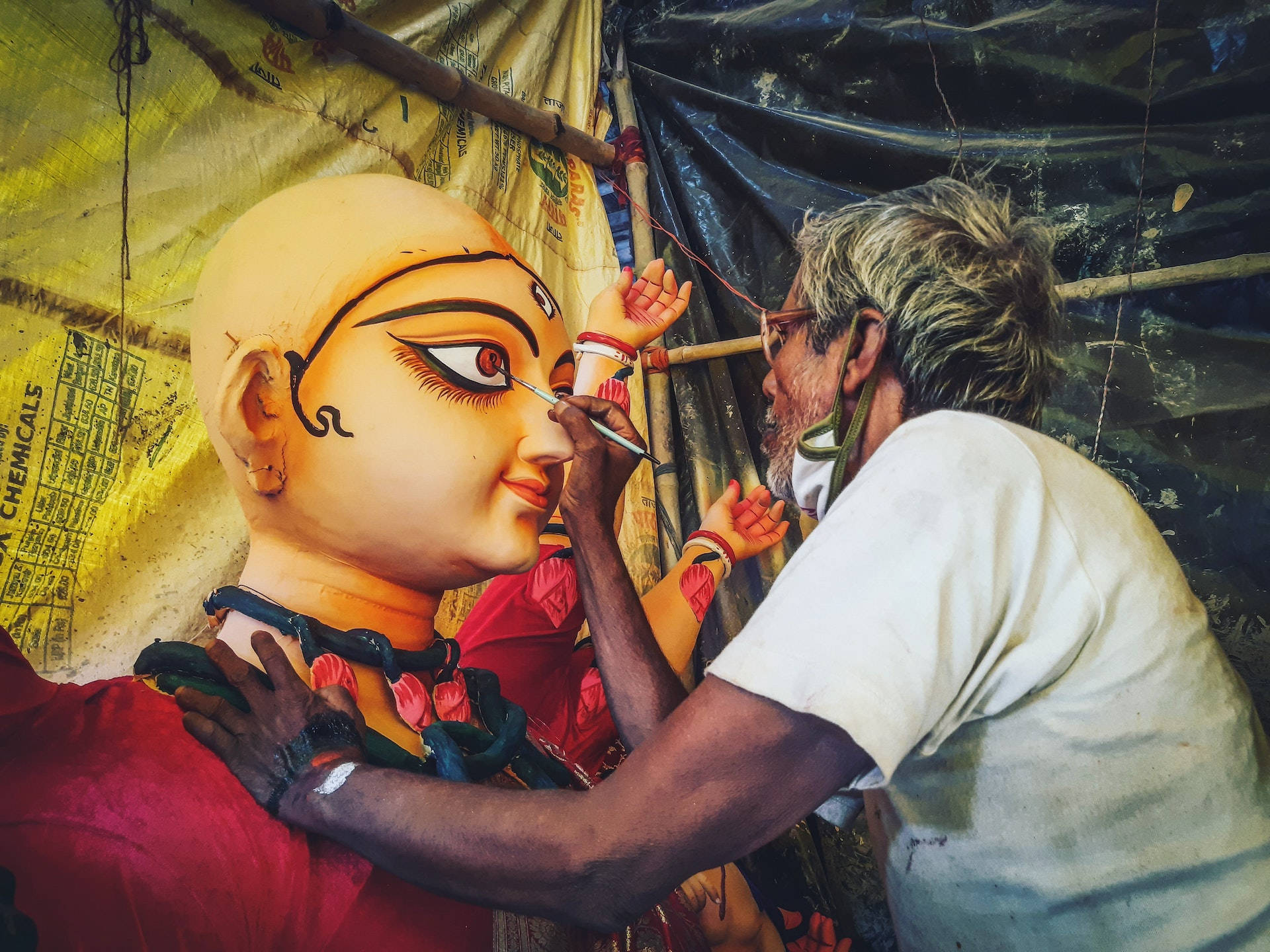Durga 桌布 壁紙 — 工匠在臨時黃色帆布篷下，一絲不苟地為大型神像繪製精細的眼睛。