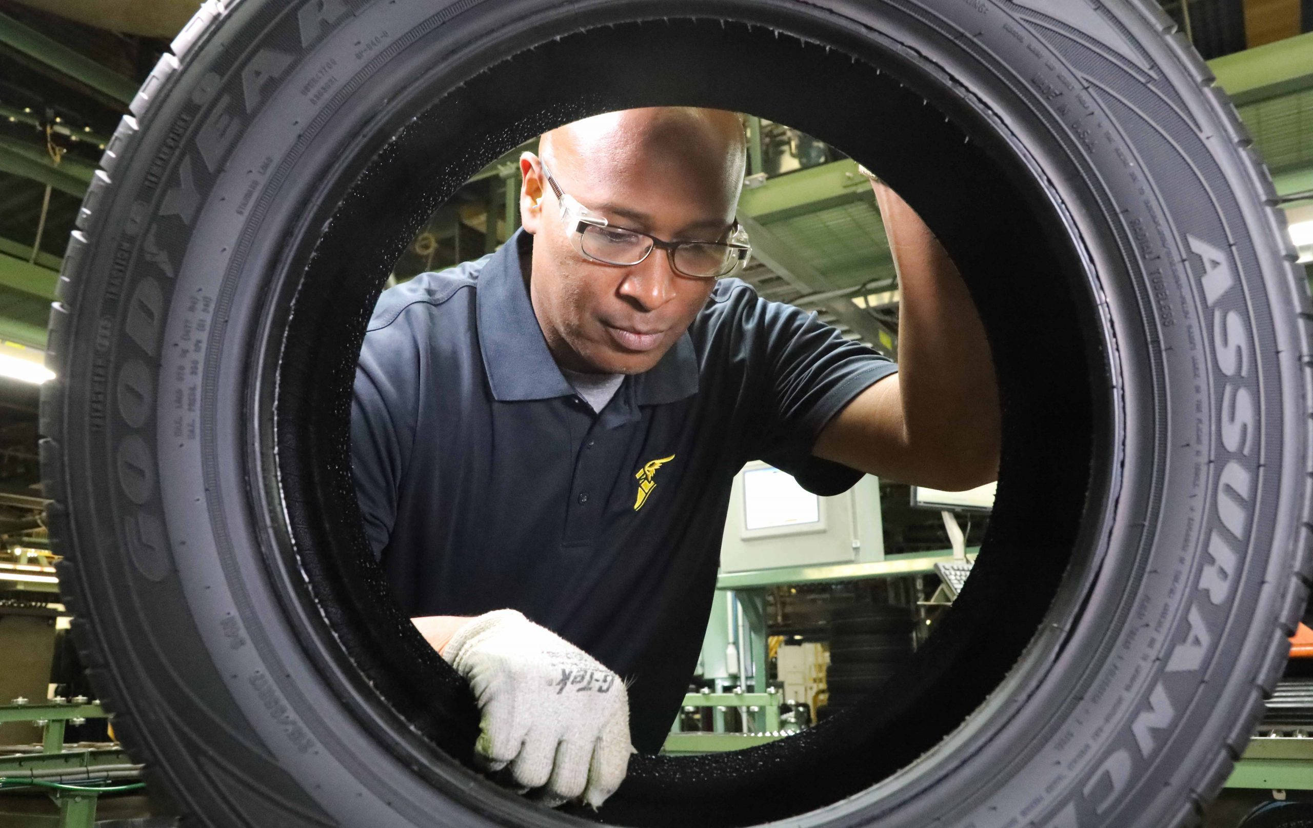 人物 桌布 壁紙 — 工廠工人正透過圓形開口檢查一個大型的Goodyear Assurance輪胎。