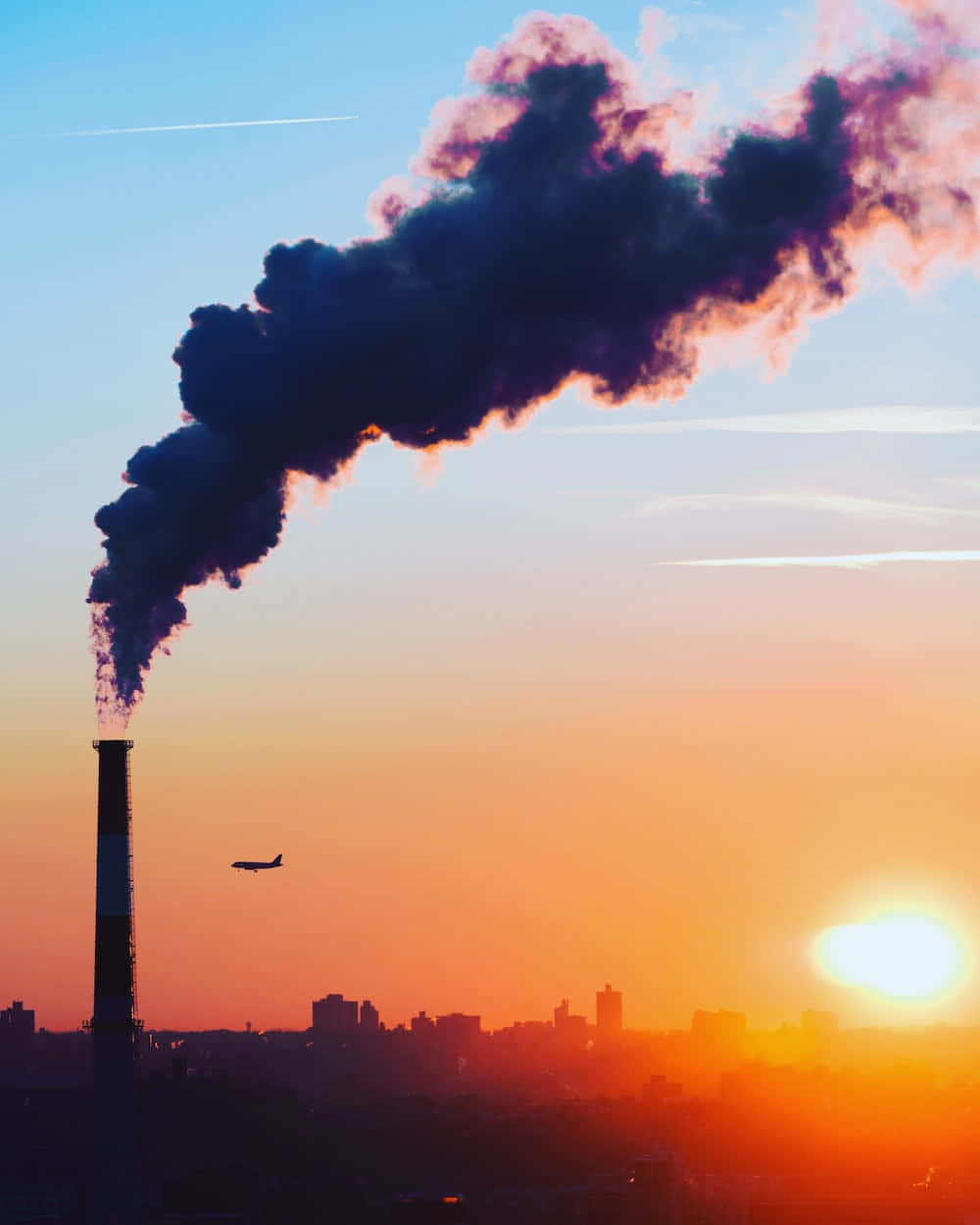 Polluting 桌布 壁紙 — 工廠煙囪在鮮豔的橙色日落天空下排放濃厚的黑煙，遠處有一架飛機飛越城市天際線。
