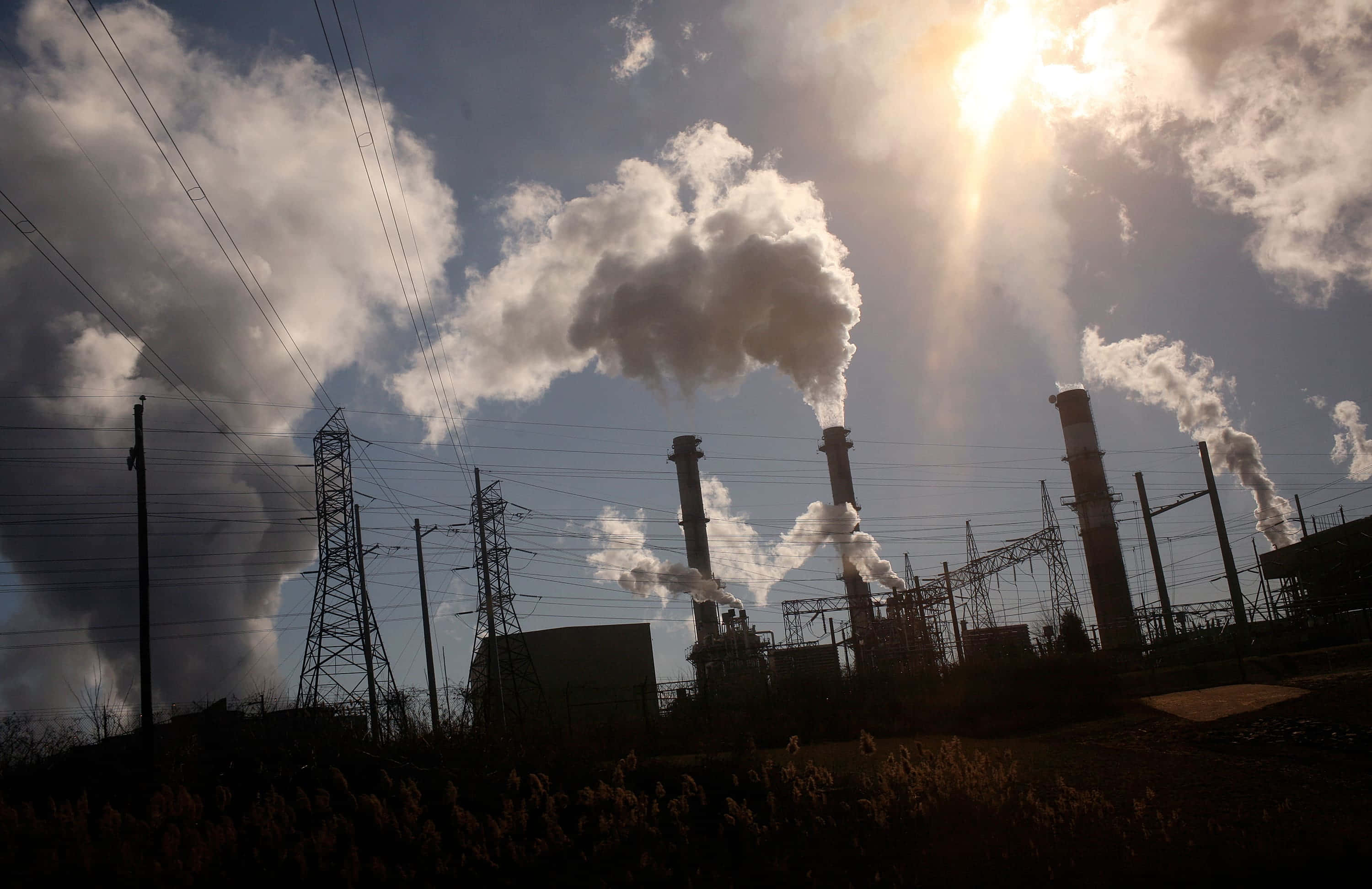 Pollution 桌布 壁紙 — 工業煙囪在明亮的陽光天空下排放濃厚的煙霧，頭頂上有電線縱橫交錯。