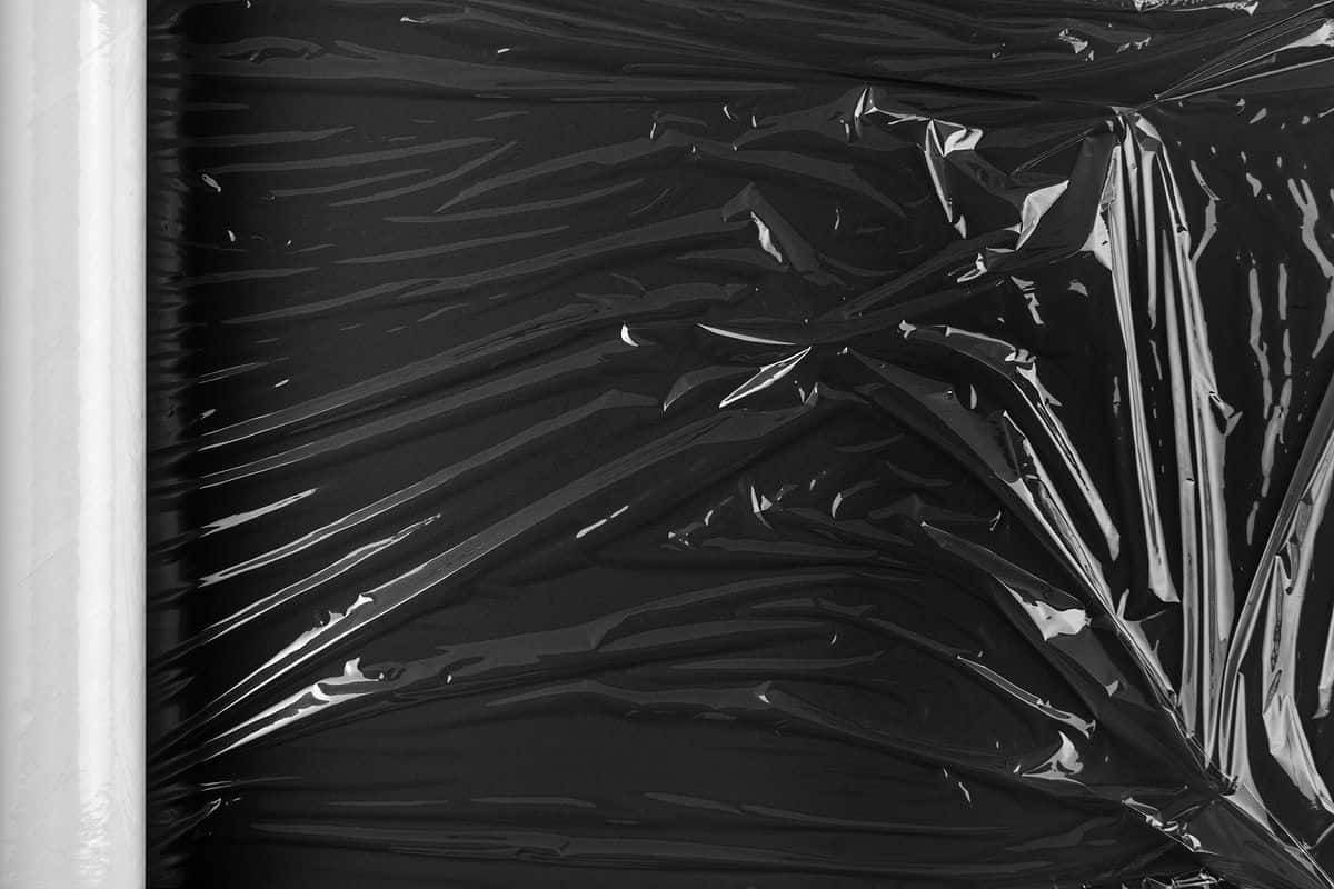 Plastic 桌布 壁紙 — 左側有白色卷邊、帶有光澤高光的皺巴巴黑色保鮮膜的特寫。