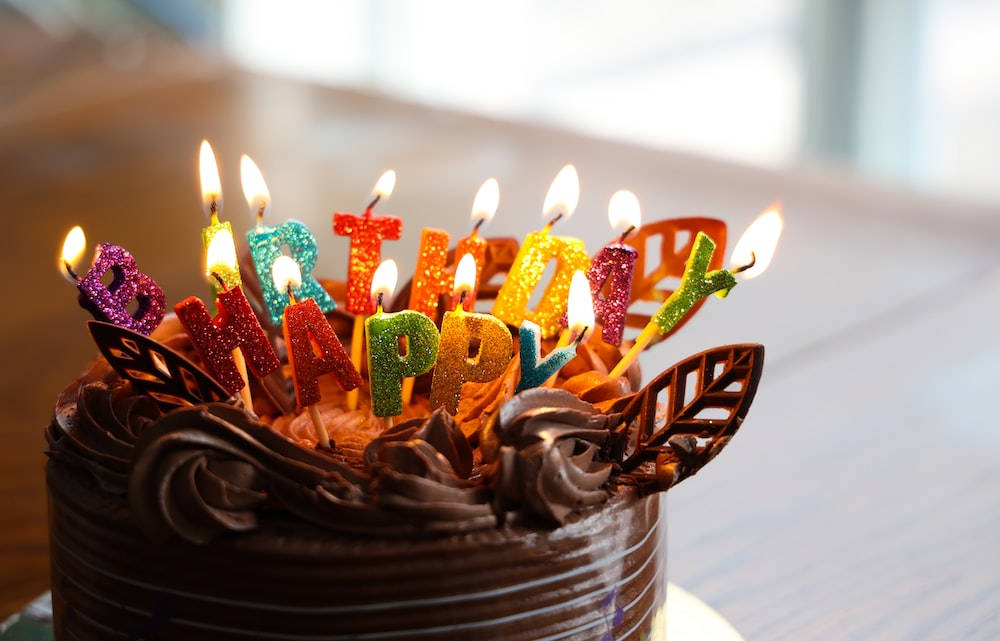 Birthday 桌布 壁紙 — 巧克力生日蛋糕特寫，上面有色彩繽紛閃爍的蠟燭拼出「HAPPY BIRTHDAY」字樣，並燃點著火焰。