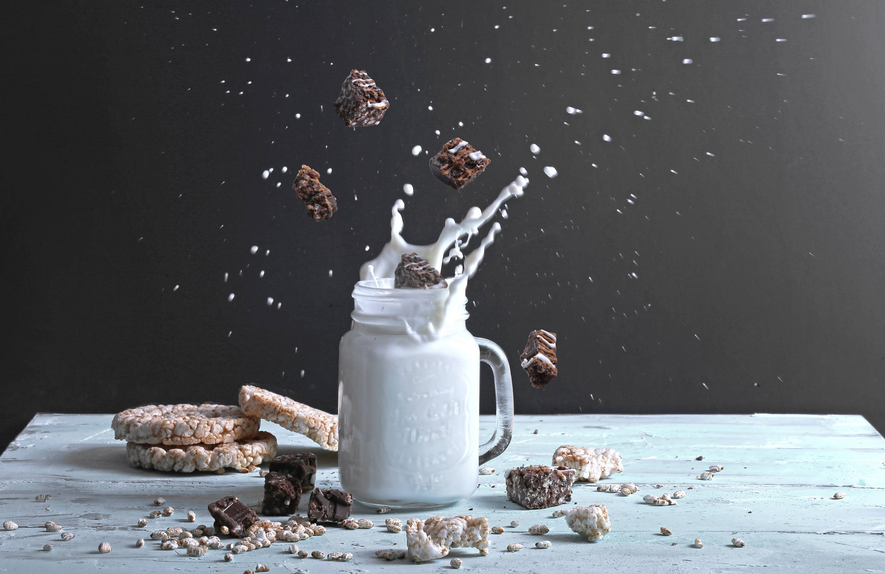 Milk 桌布 壁紙 — 巧克力米香脆片點心在玻璃罐中爆炸成泡沫狀的牛奶飛濺，背景為深色。