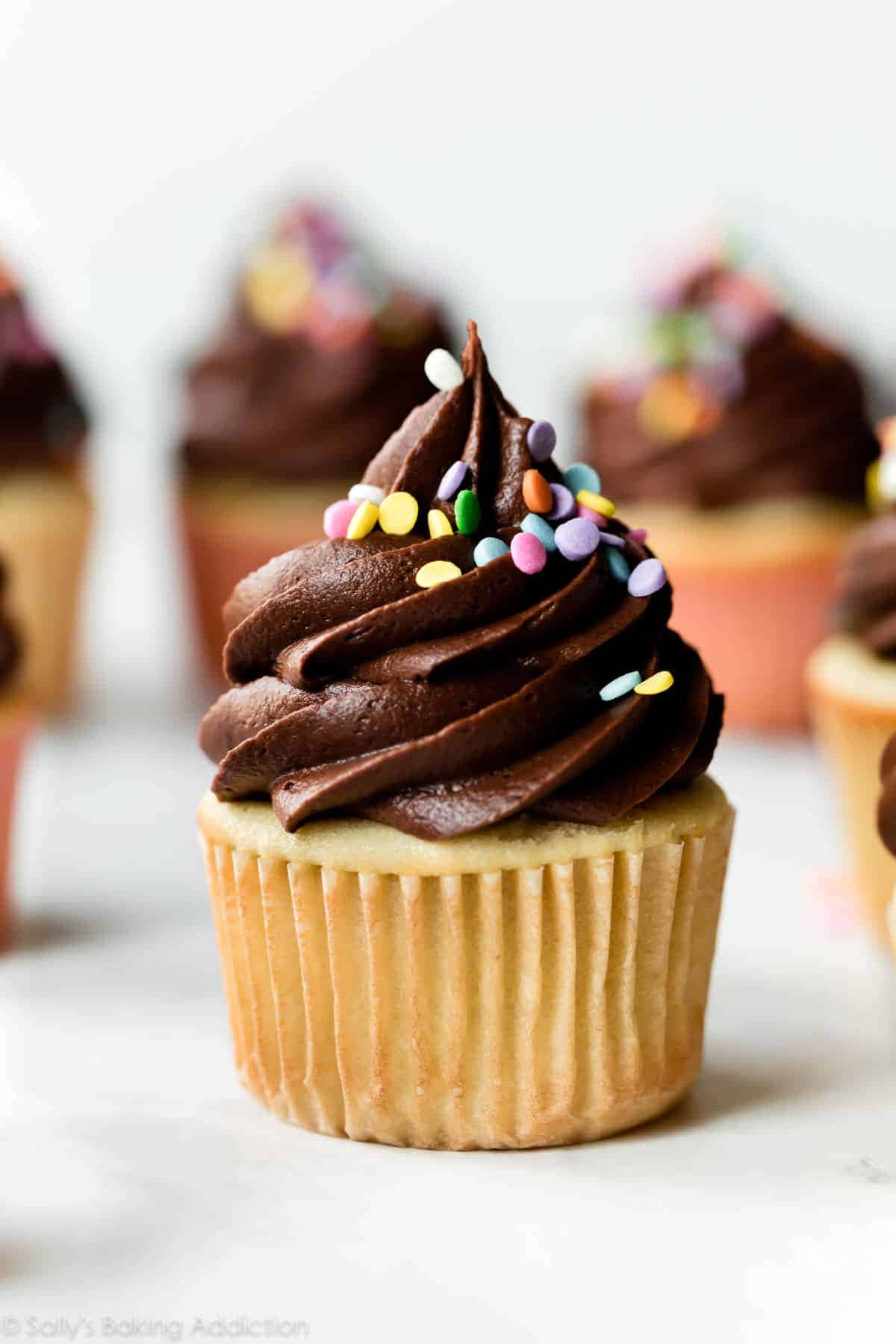 Cupcake 桌布 壁紙 — 巧克力糖霜杯子蛋糕的特寫，上面有彩色糖粒，放在大理石表面上。