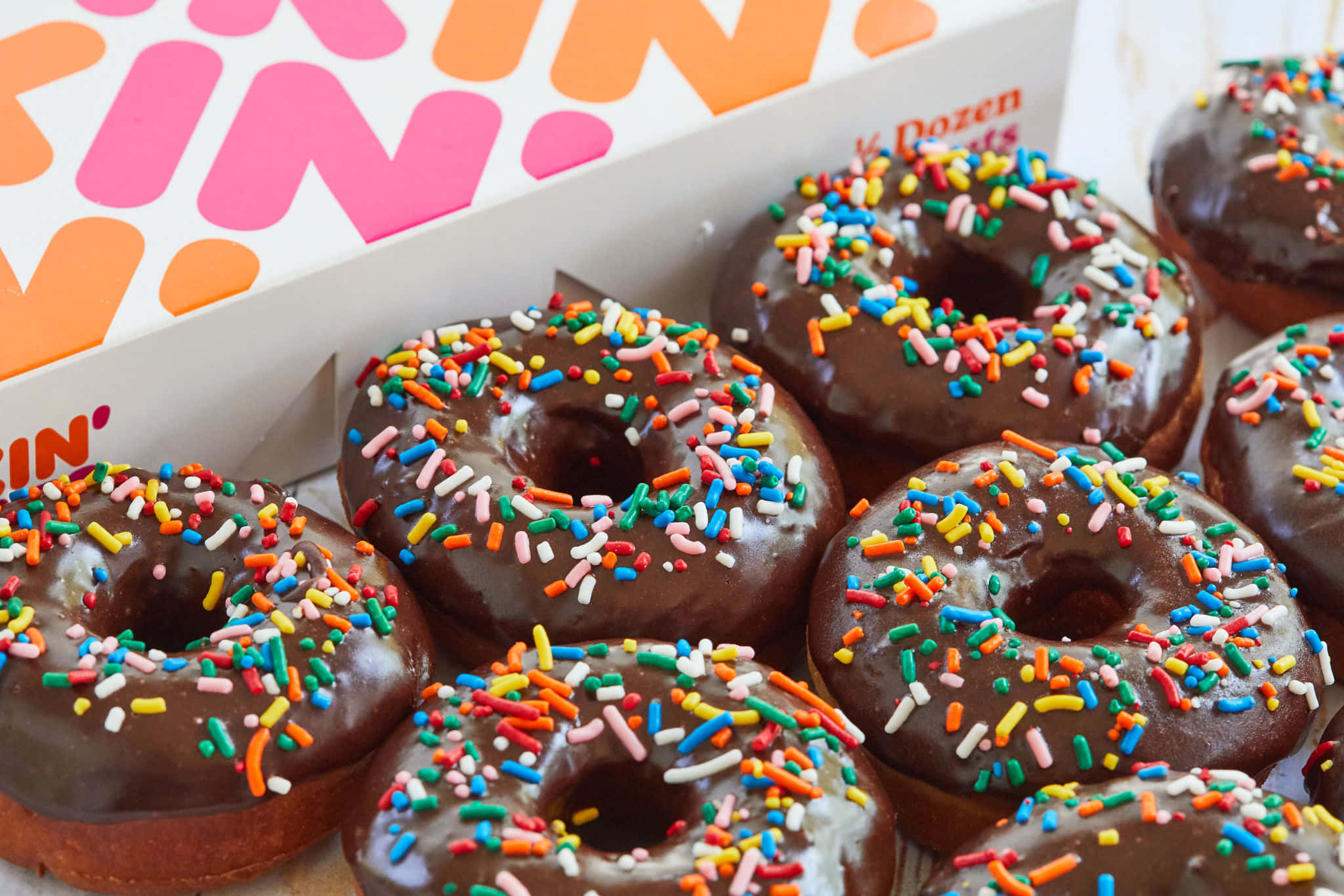 Glazed Donut 桌布 壁紙 — 巧克力糖霜甜甜圈上面灑滿彩色糖粒，從品牌盒子中傾瀉而出的特寫。