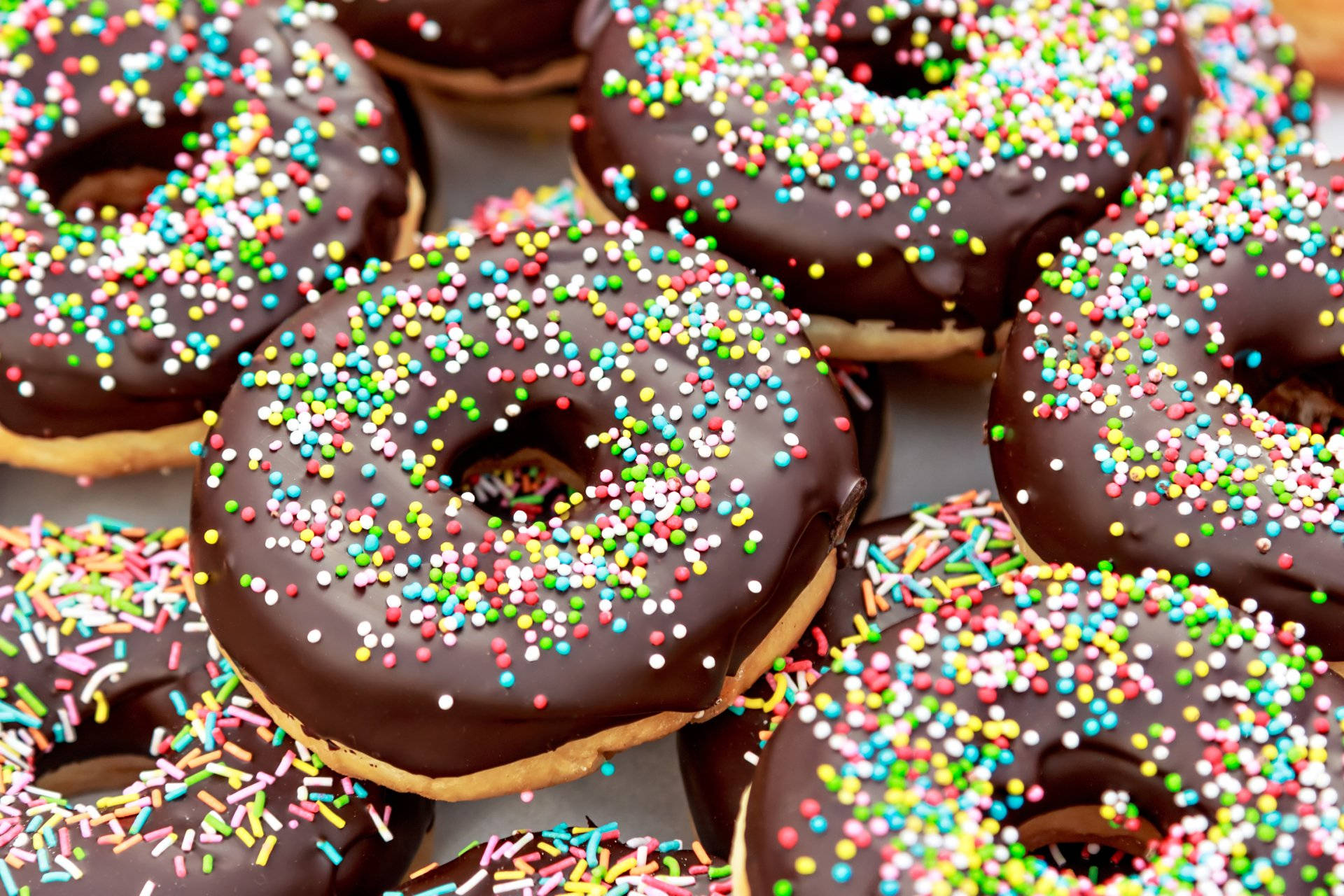 Donut 桌布 壁紙 — 巧克力糖霜甜甜圈的近照，上面鋪滿了色彩繽紛的彩虹糖粒。