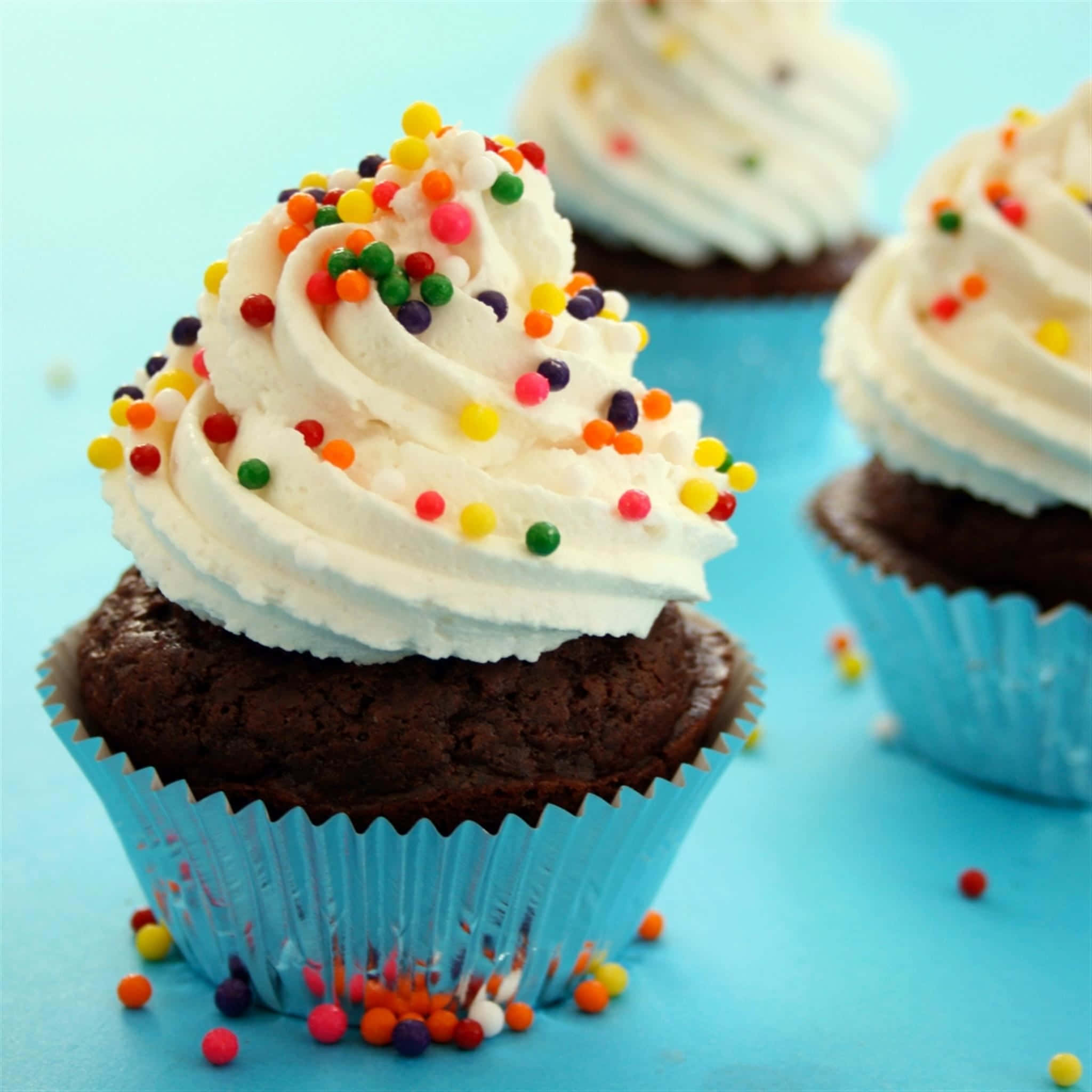 Cupcake 桌布 壁紙 — 巧克力紙杯蛋糕的特寫，上面有白色糖霜和彩色糖針，放在亮藍色表面上。