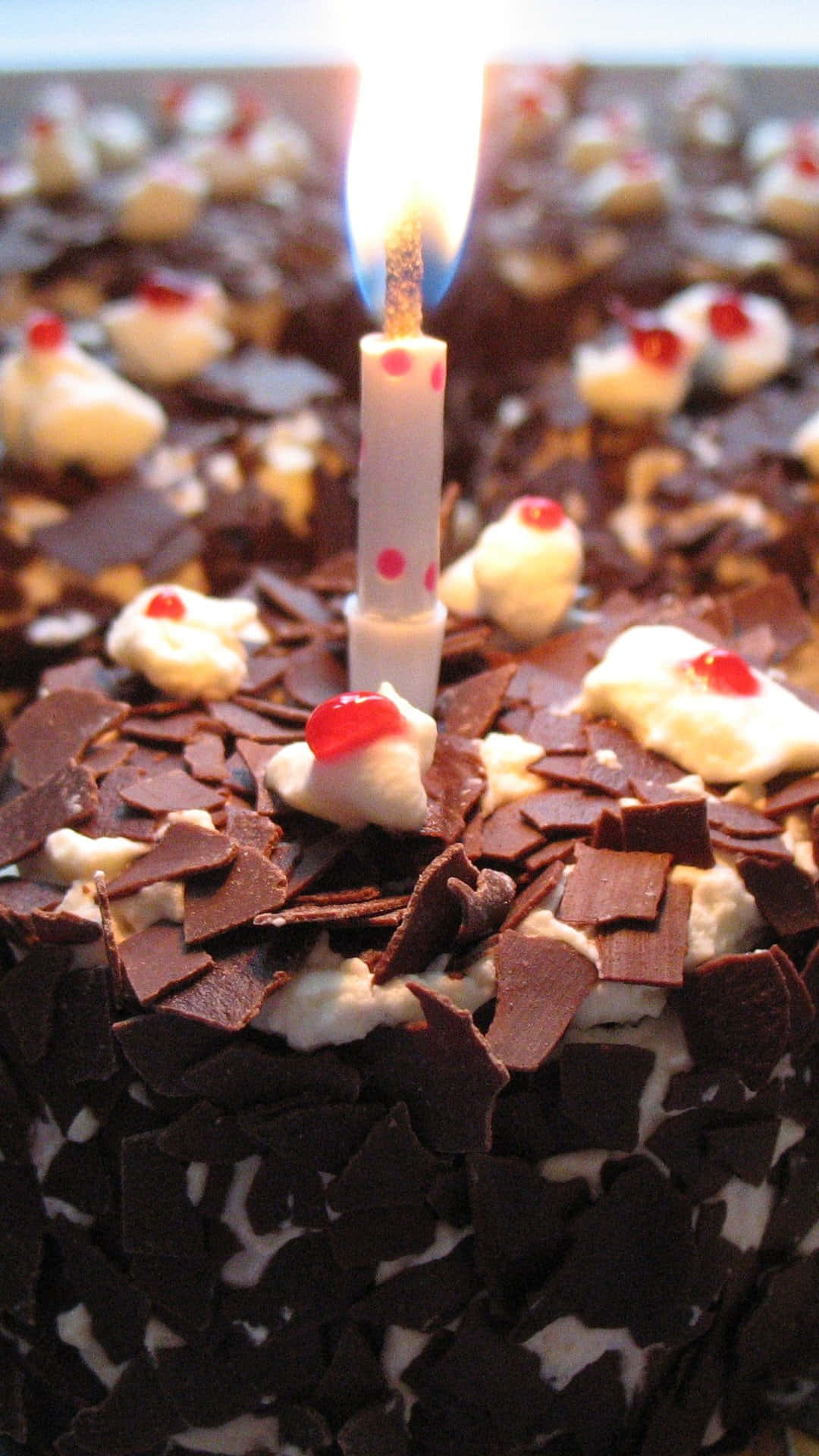Black Forest Cake 桌布 壁紙 — 巧克力蛋糕的特寫，上面有鮮奶油、櫻桃切片和一支有粉紅色圓點的點燃蠟燭。