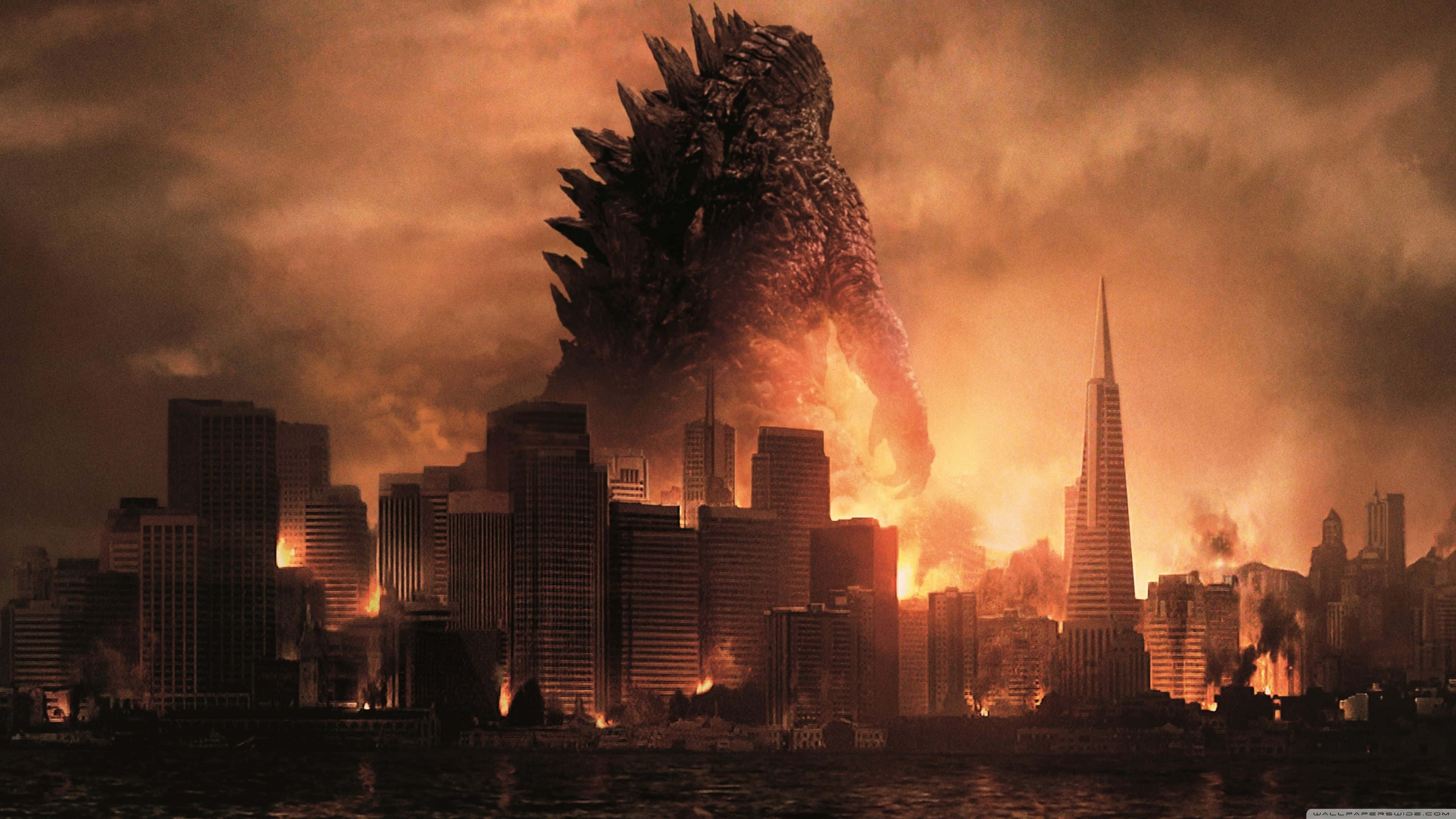 Burning Godzilla 桌布 壁紙 — 巨型哥吉拉聳立在夕陽下燃燒的城市景觀之上，火焰和煙霧從被摧毀的摩天大樓中升起。