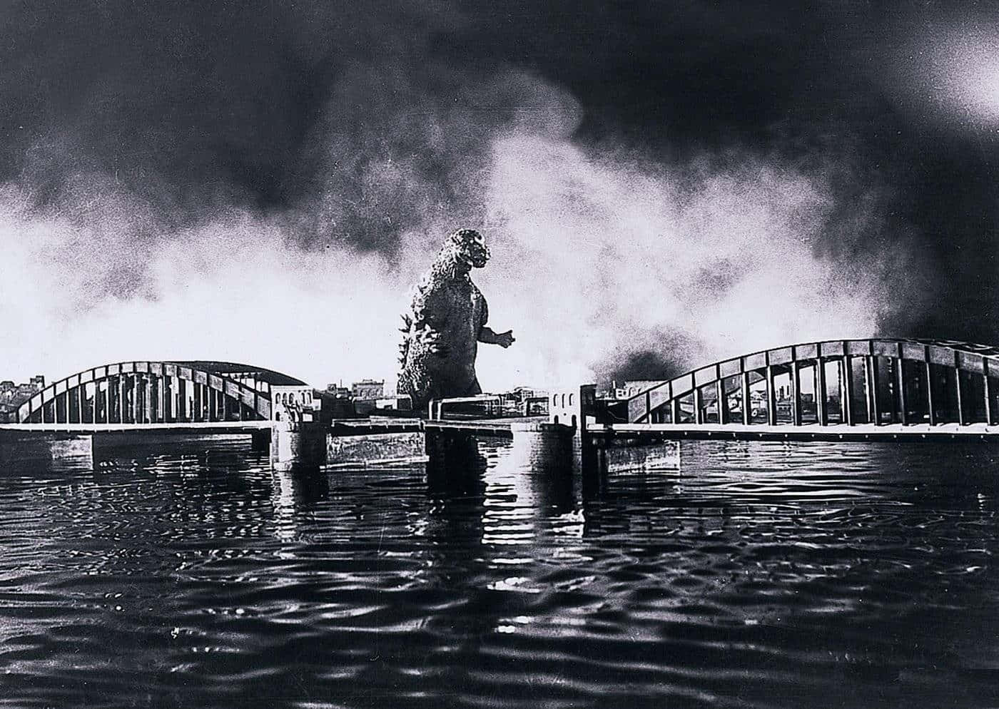 Classic Godzilla 桌布 壁紙 — 巨型怪獸哥吉拉站在水中，周圍是斷橋，身後濃煙滾滾，形成戲劇性的黑白場景。