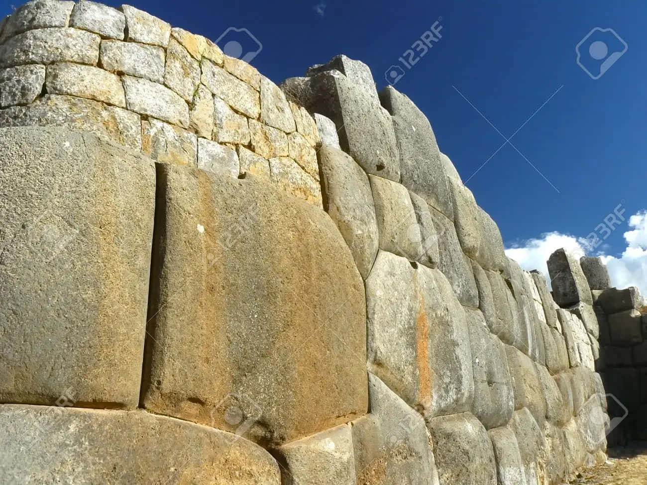 Attraction 桌布 壁紙 — 巨大的古代石塊在晴朗的藍天和散落的雲朵下形成高聳的印加牆。