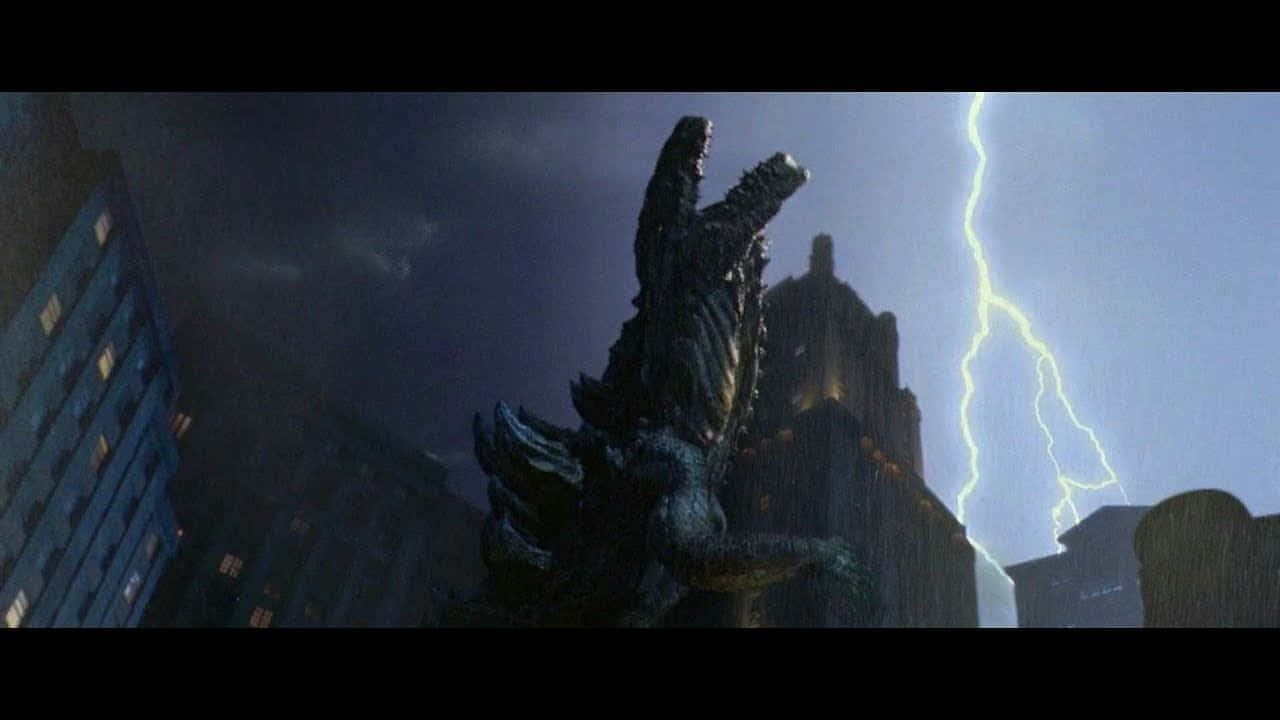 godzilla 1998 桌布 壁紙 — 巨大的哥吉拉在暴風雨的城市景觀中咆哮，閃電擊中高聳的摩天大樓背後。