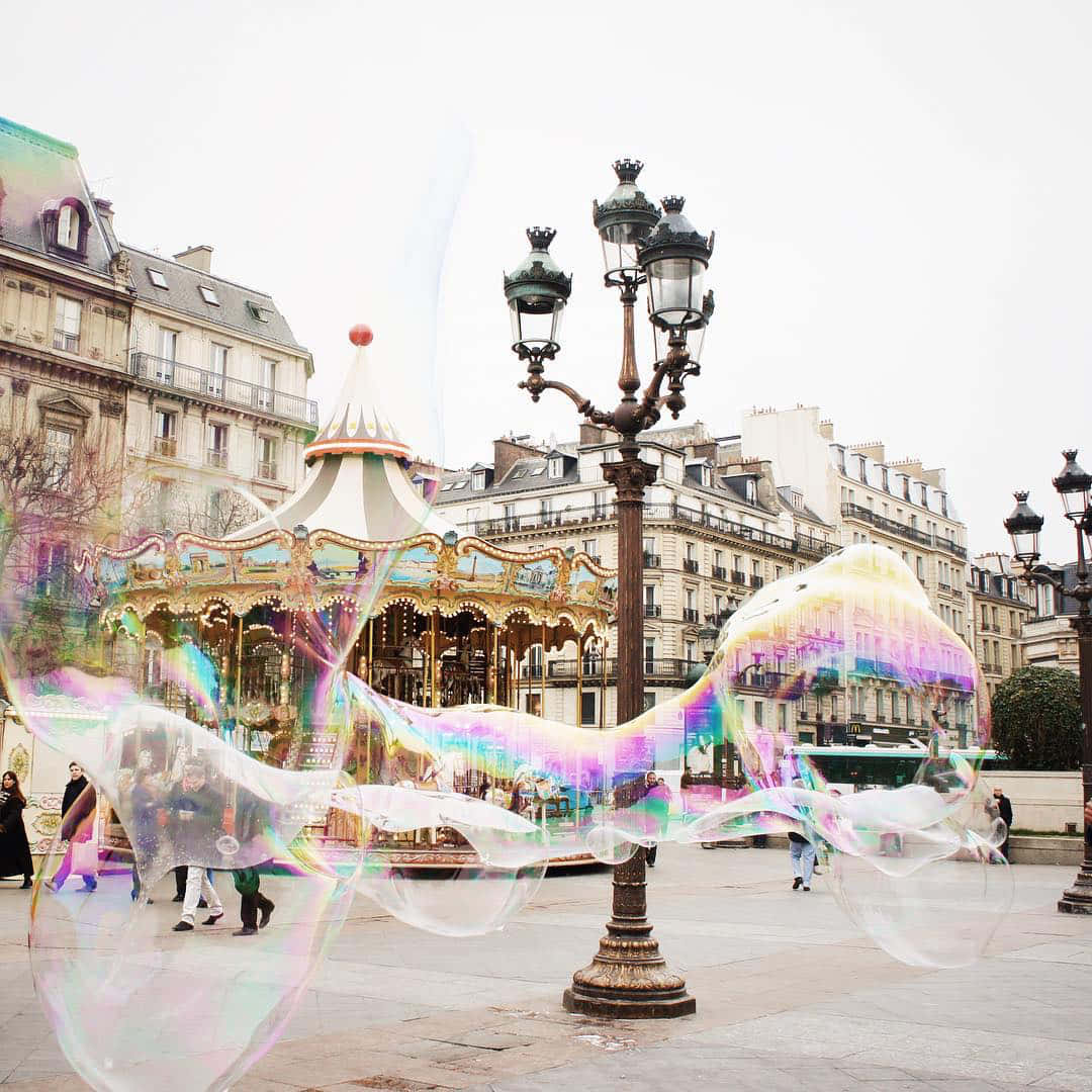 Bubbles 桌布 壁紙 — 巨大的彩虹色肥皂泡在繁忙廣場上的經典巴黎旋轉木馬上優雅地漂浮。