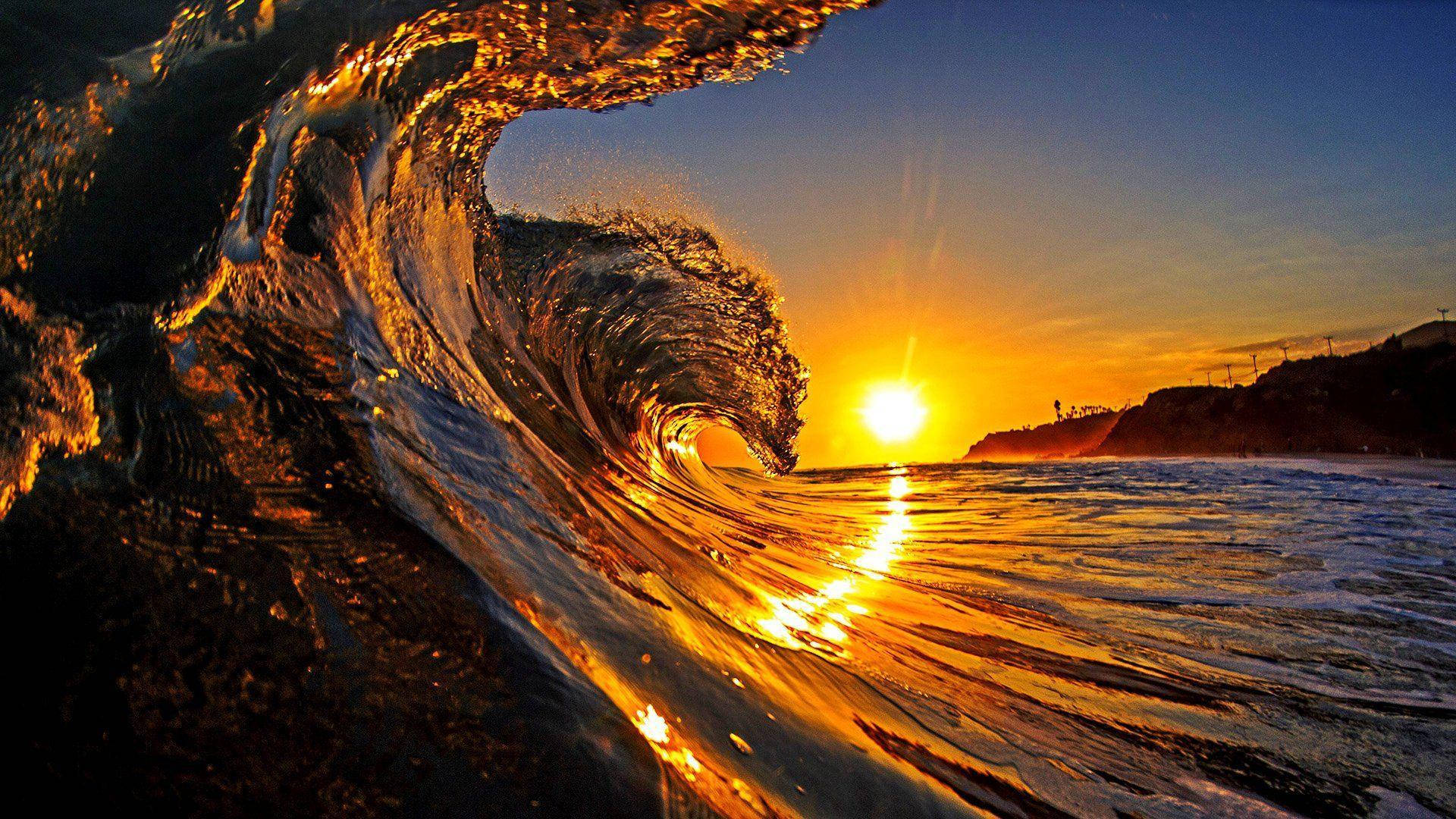日出 桌布 壁紙 — 巨大的海浪在日落時捲起，金色光線在其濕潤表面反射，映襯著鮮豔的橙色和藍色天空。