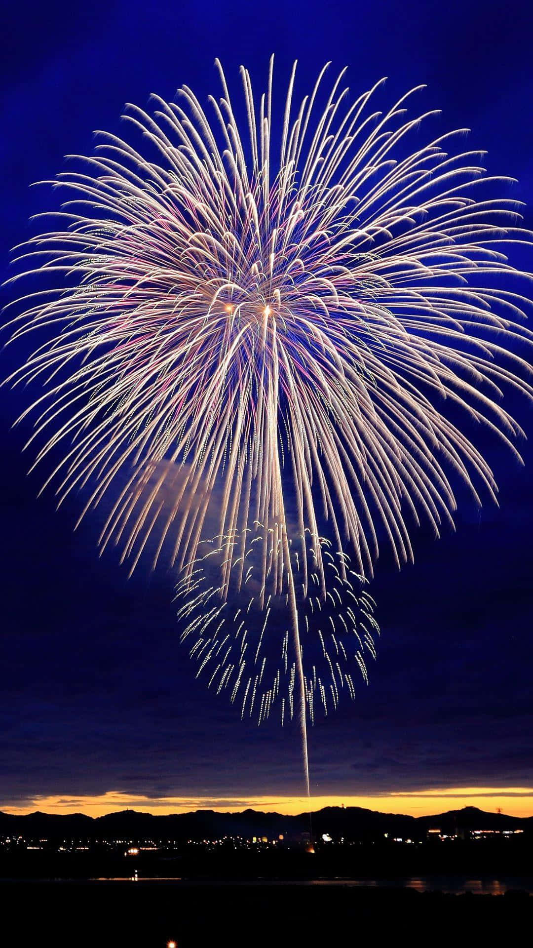 Fireworks 桌布 壁紙 — 巨大的白色和金色煙火爆炸在深藍色夜空中綻放，下方是剪影般的山脈和閃爍的城市燈光。