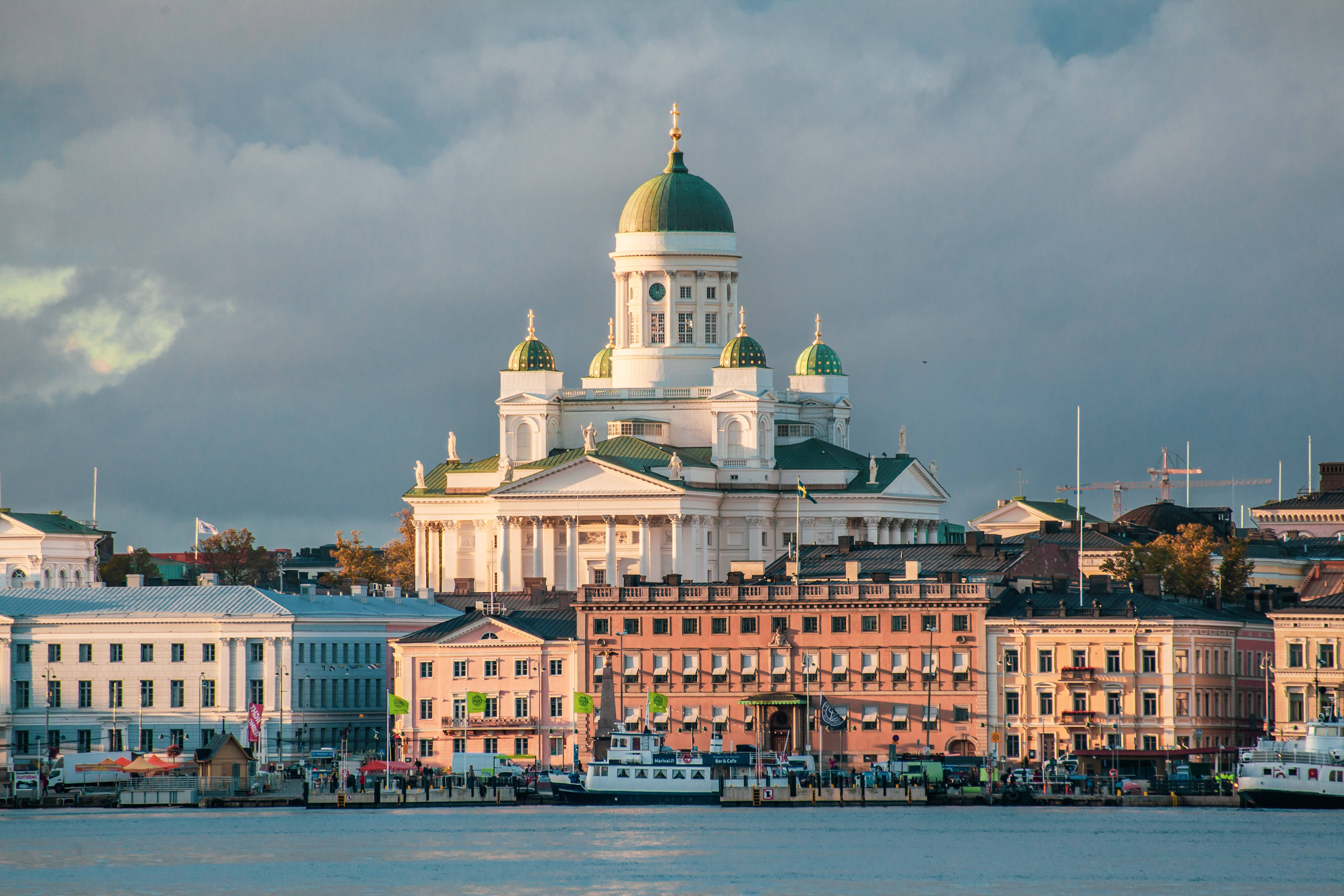 Finland 桌布 壁紙 — 巨大的白色大教堂，綠色圓頂，聳立在色彩繽紛的歷史建築之上，沿著平靜的海濱，天空多雲。