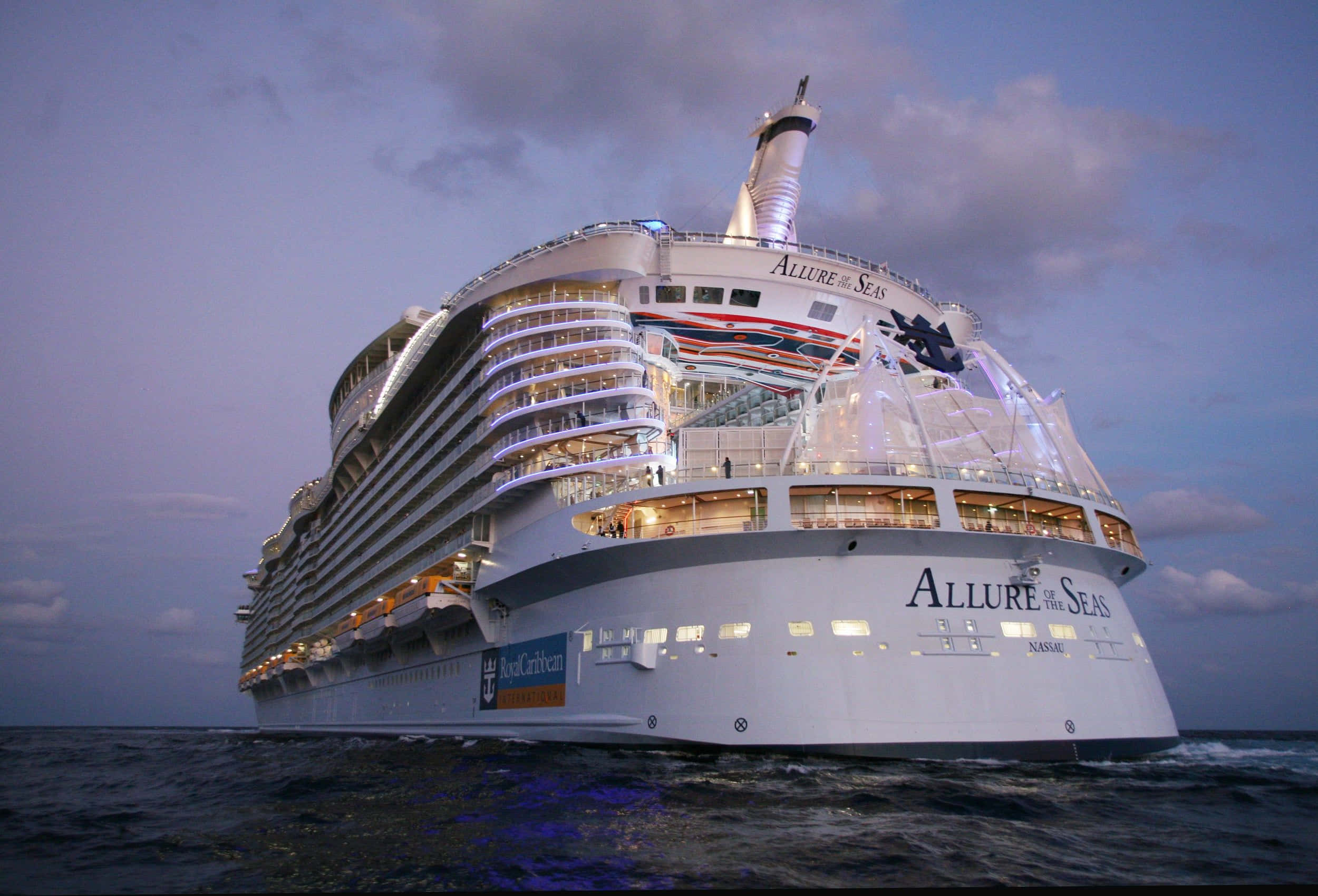 Carnival Vista 桌布 壁紙 — 巨大的皇家加勒比Allure of the Seas郵輪在昏暗的紫色天空下閃爍著溫暖的燈光，在平靜的海面上航行。