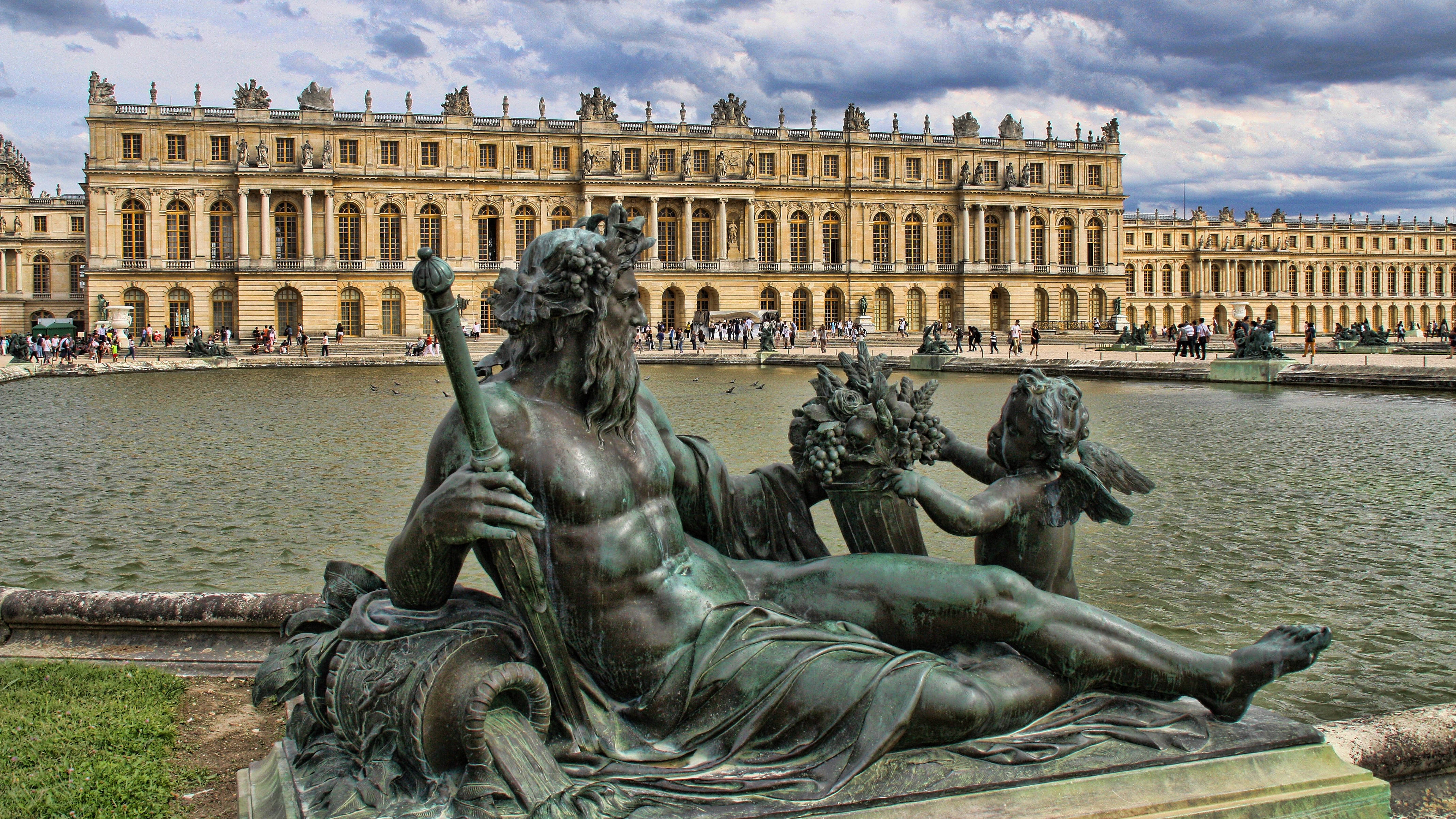 France 桌布 壁紙 — 巨大的神話人物青銅雕像在凡爾賽宮前倒映的池塘邊休憩，天空戲劇性地多雲。