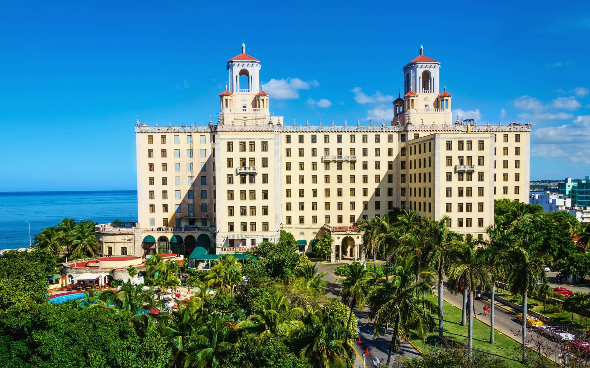 Cuba 桌布 壁紙 — 巨大的米色雙塔飯店雄偉地矗立在海洋邊，天空湛藍，點綴著蓬鬆的白雲。