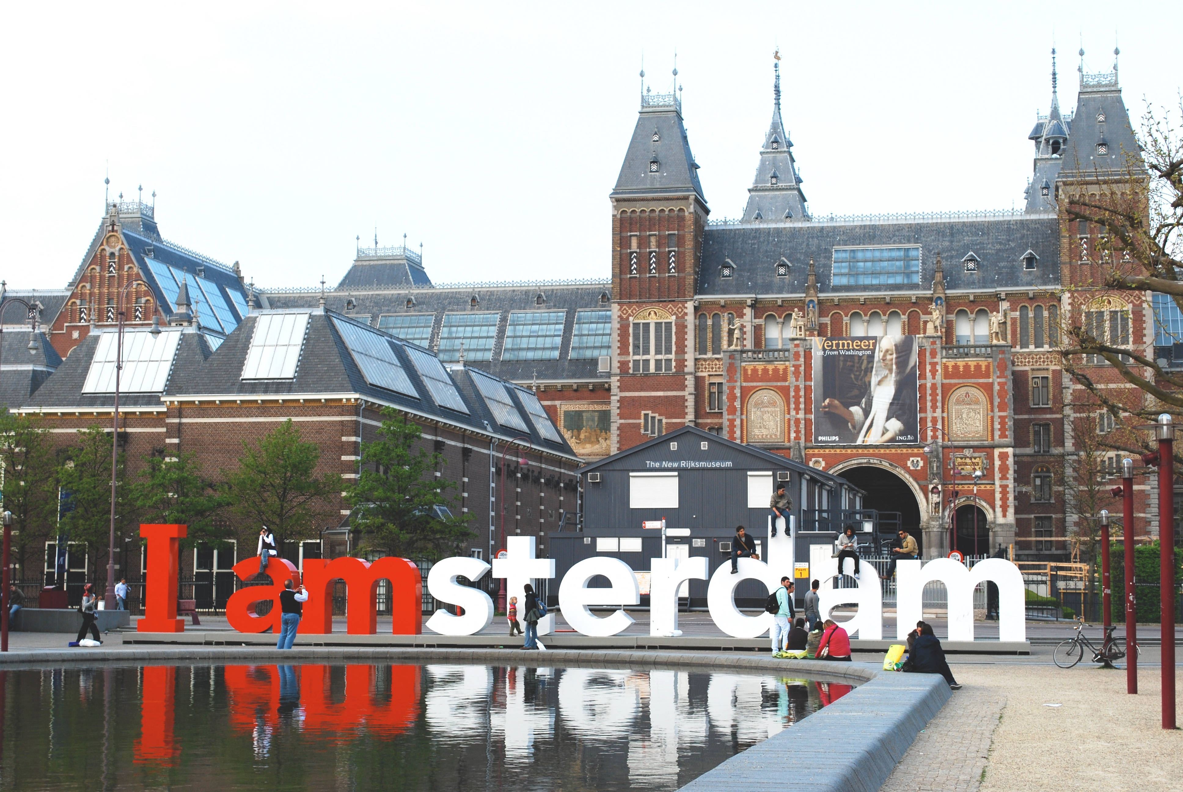Netherlands 桌布 壁紙 — 巨大的紅色和白色 'I amsterdam' 字母矗立在歷史悠久的國立博物館前，附近的人們正在休憩。