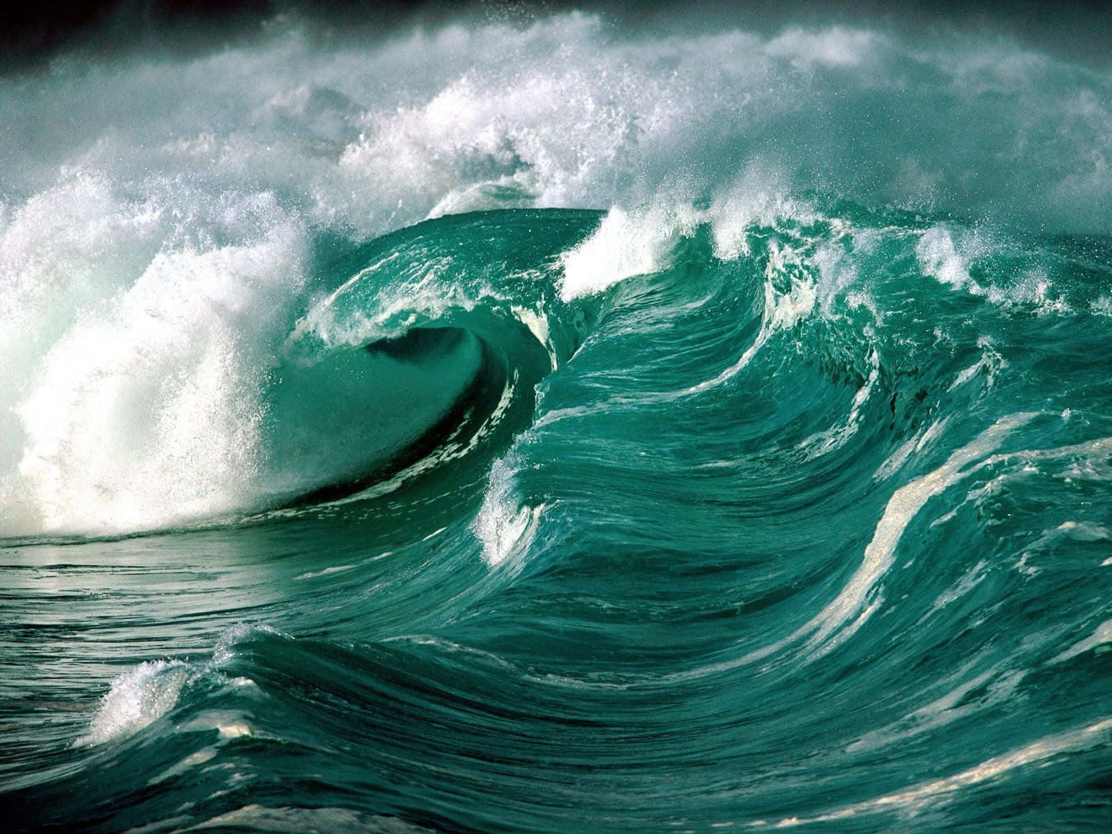 Ocean Waves 桌布 壁紙 — 巨大的藍綠色海浪強力翻捲，白色泡沫在黑暗暴風雨的天空中飛濺。