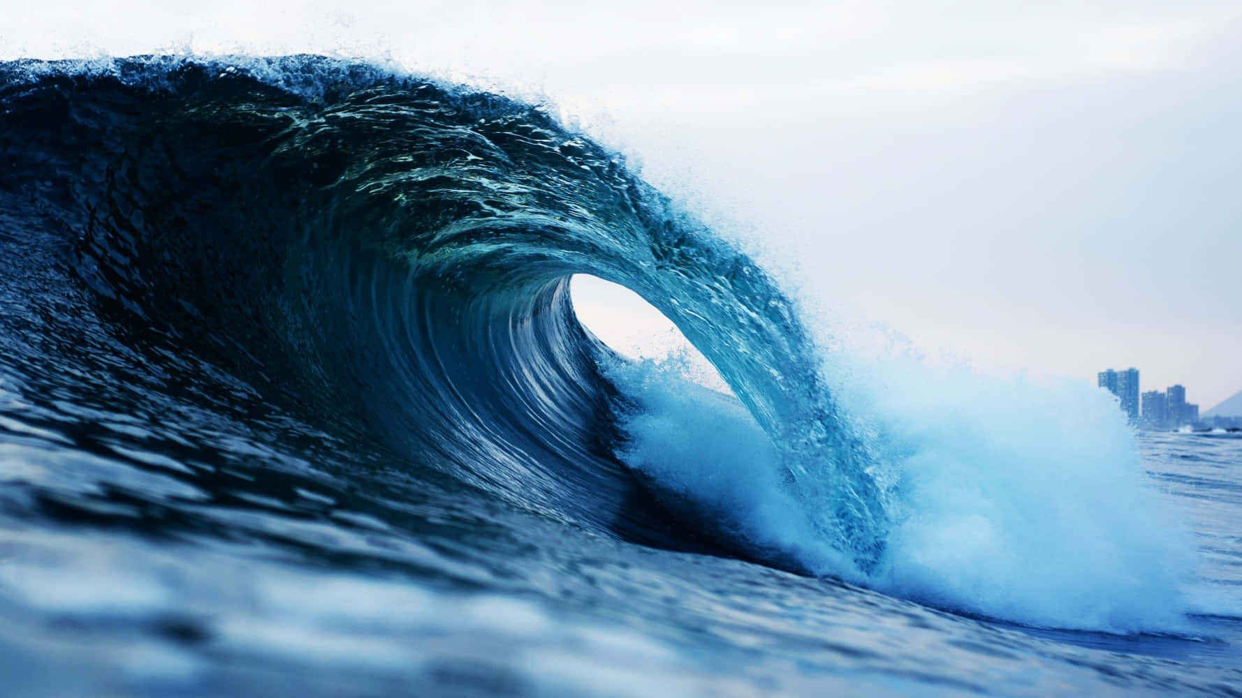 Wave 桌布 壁紙 — 巨大的藍綠色海浪捲成完美的桶狀，透過其空心可以看到城市天際線。