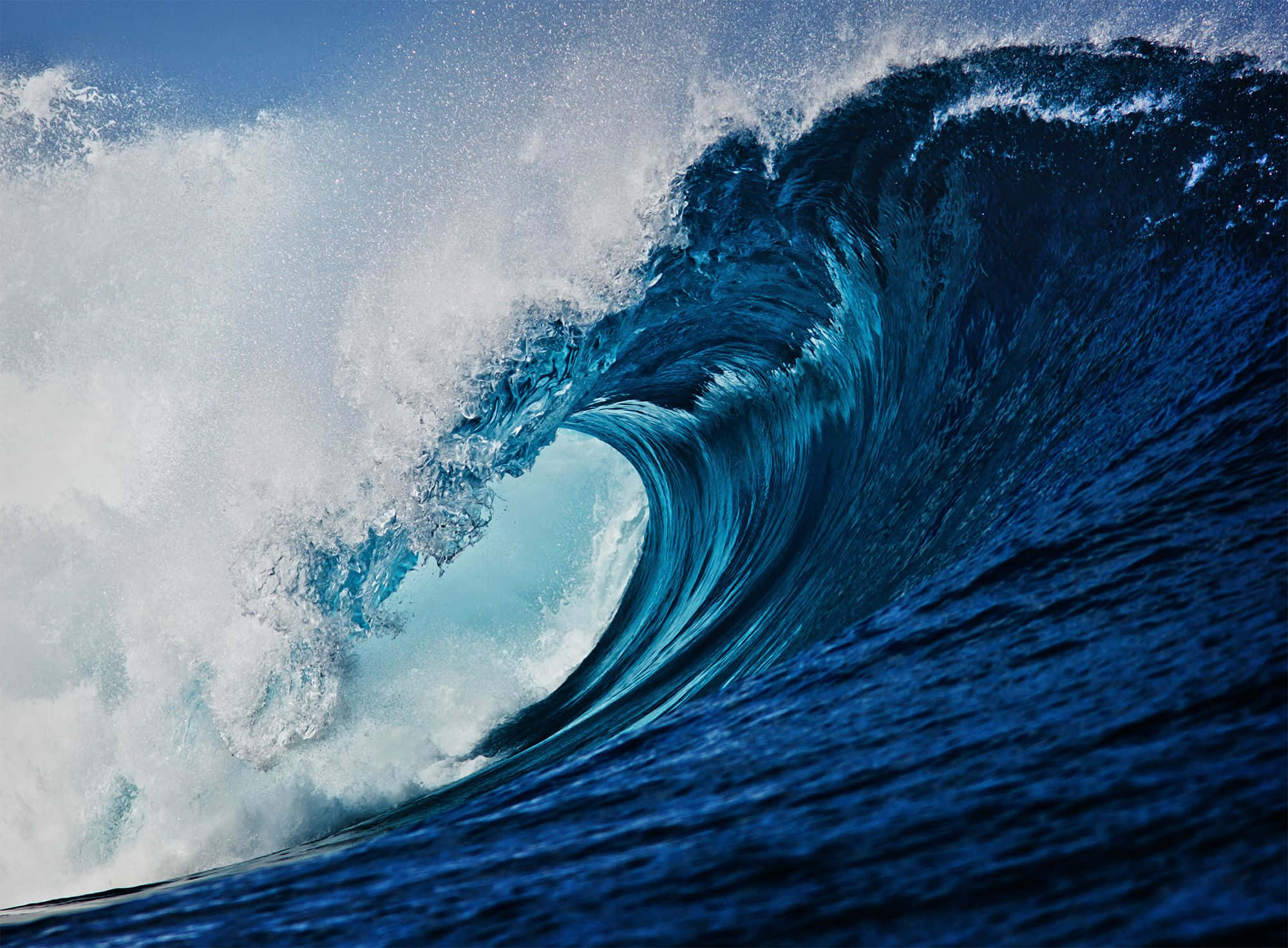 waves 桌布 壁紙 — 巨大的藍綠色海浪捲成完美的筒狀，伴隨著泡沫般的白色浪花，映襯著清澈的藍天。