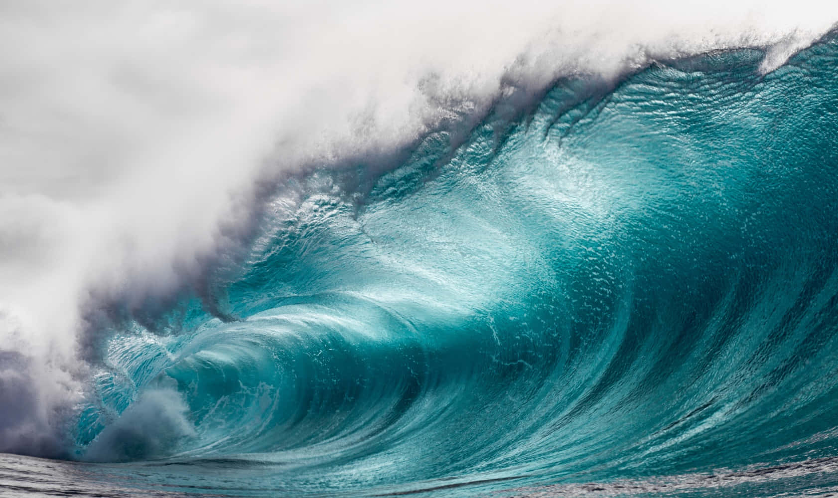 Wave 桌布 壁紙 — 巨大的藍綠色海浪捲成完美的筒狀，帶著泡沫般的白色浪花，映襯著多雲的天空。