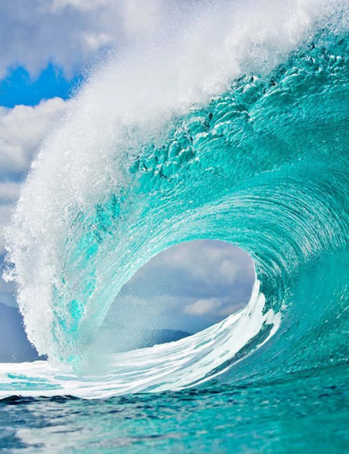 Wave 桌布 壁紙 — 巨大的藍綠色海浪捲成完美的管浪，衝浪者在明亮的藍天下在其面上衝浪。
