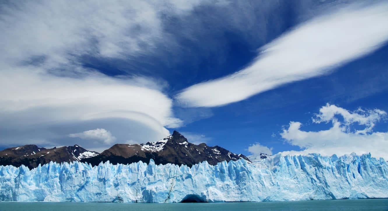Patagonia 桌布 壁紙 — 巨大的藍色冰川牆從碧綠色的水中升起，天空戲劇性，有旋轉的白雲和深藍色斑塊。