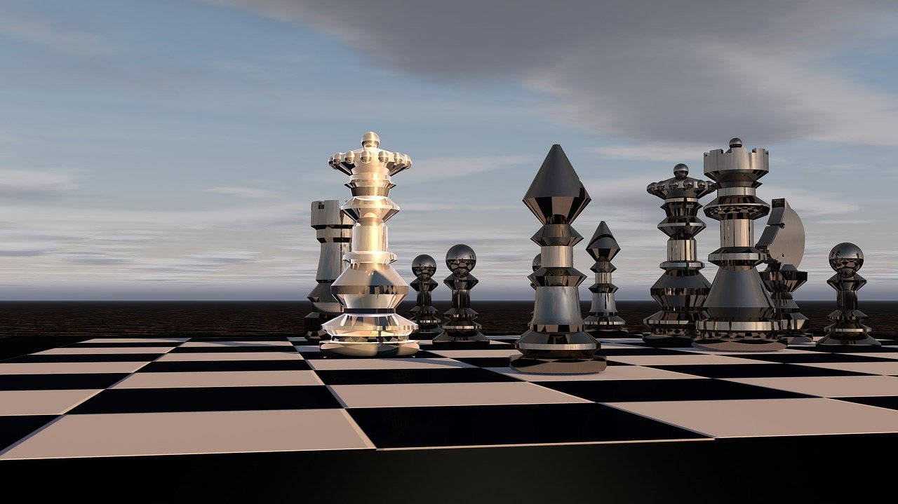 西洋棋 桌布 壁紙 — 巨大的金屬西洋棋棋子矗立在廣闊的棋盤上，背景是無盡水域上方的多雲天空。