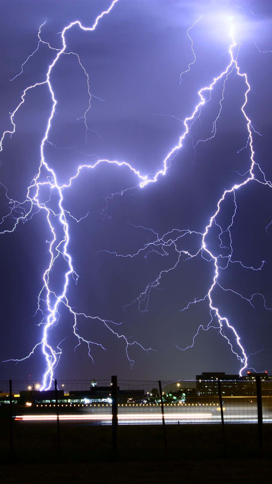 閃電 桌布 壁紙 — 巨大的鋸齒狀閃電照亮了黑暗的暴風雨天空，下方是夜晚的城市景觀，燈火輝煌。