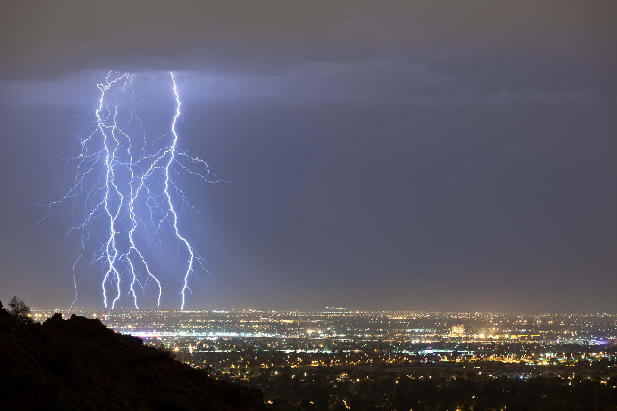 Phoenix Arizona 桌布 壁紙 — 巨大的閃電照亮了暴風雨夜晚的天空，下方是廣闊的城市景觀，閃爍著人造燈光。