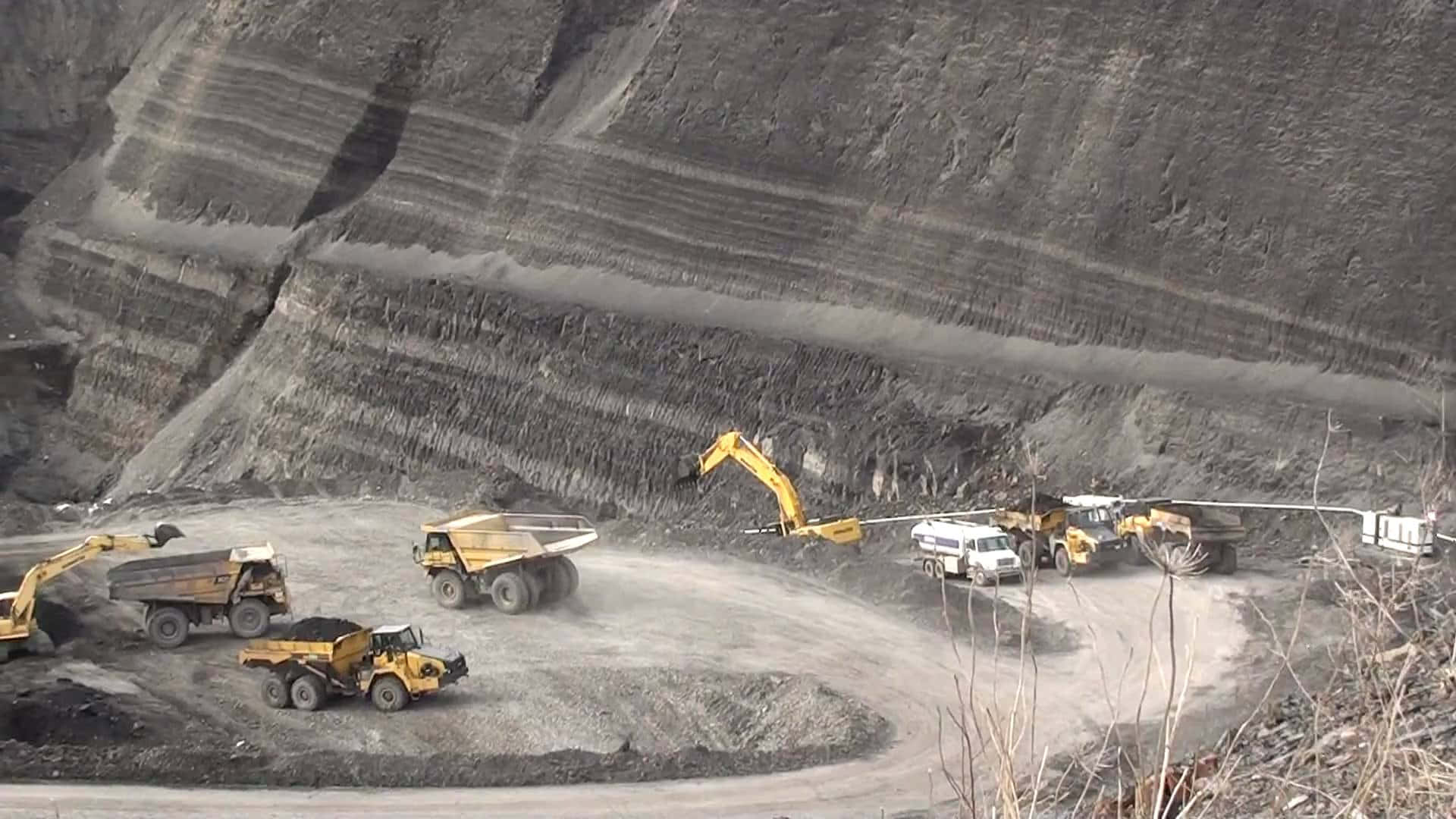 Coal Mining 桌布 壁紙 — 巨大的黃色自卸卡車和挖掘機在一個擁有梯田狀岩壁的廣闊露天礦場中作業。